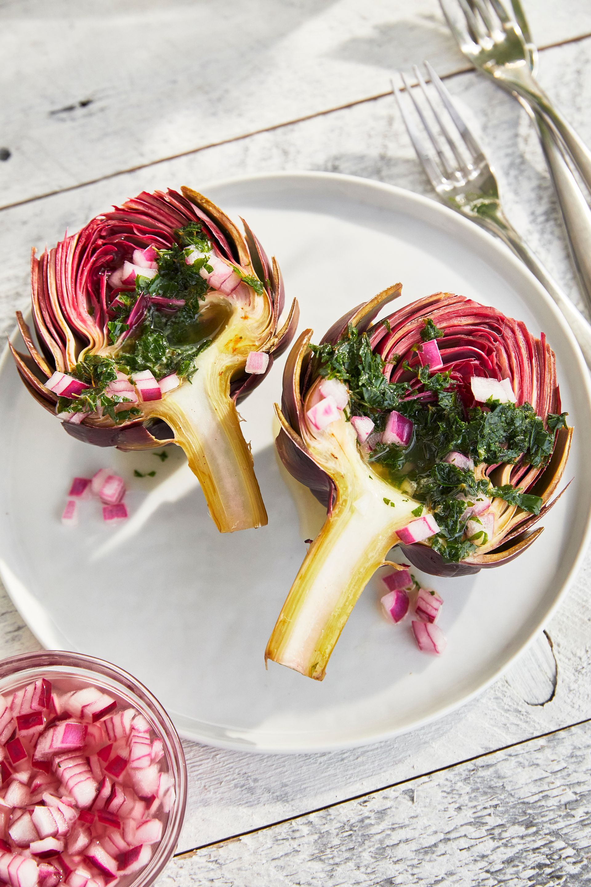 Two artichokes are sitting on a white plate on a wooden table.