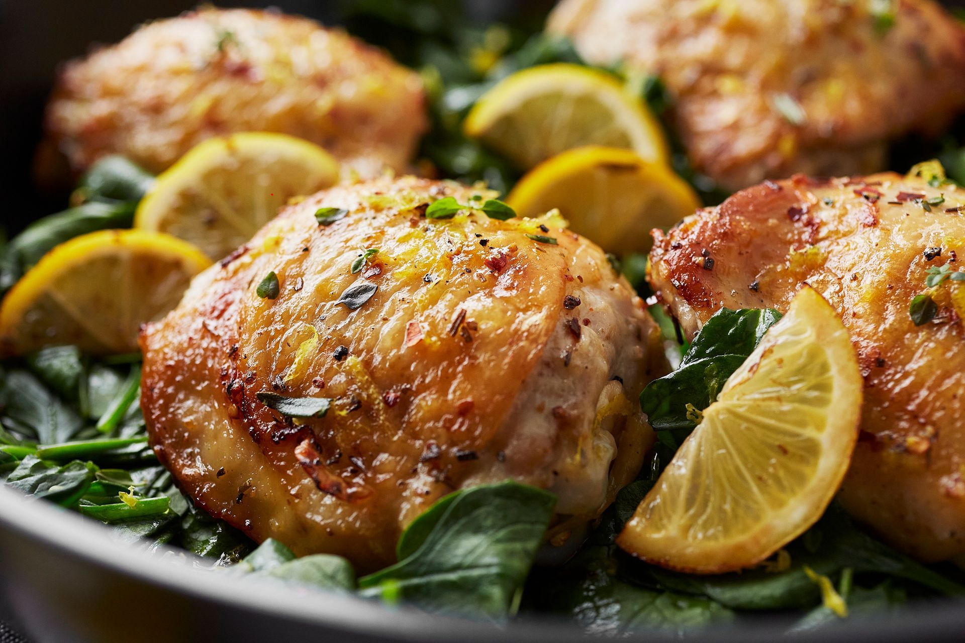 Chicken thighs with lemon slices and spinach in a pan.