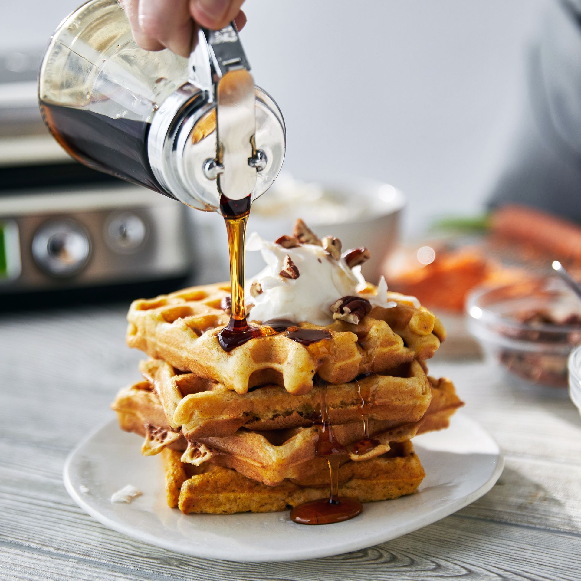 A person pouring syrup on a stack of waffles