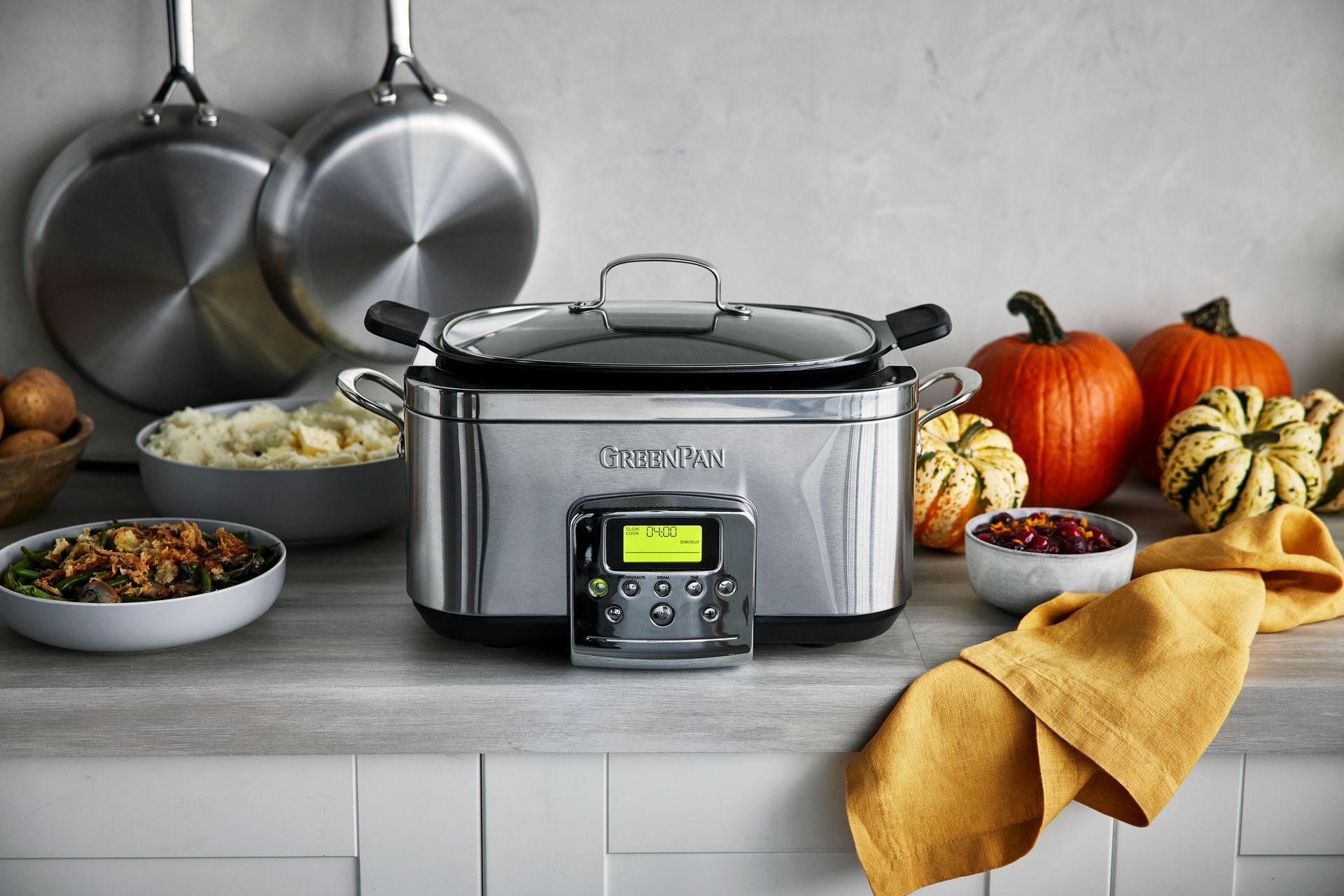 A Green Pan stainless steel slow cooker is sitting on a kitchen counter.