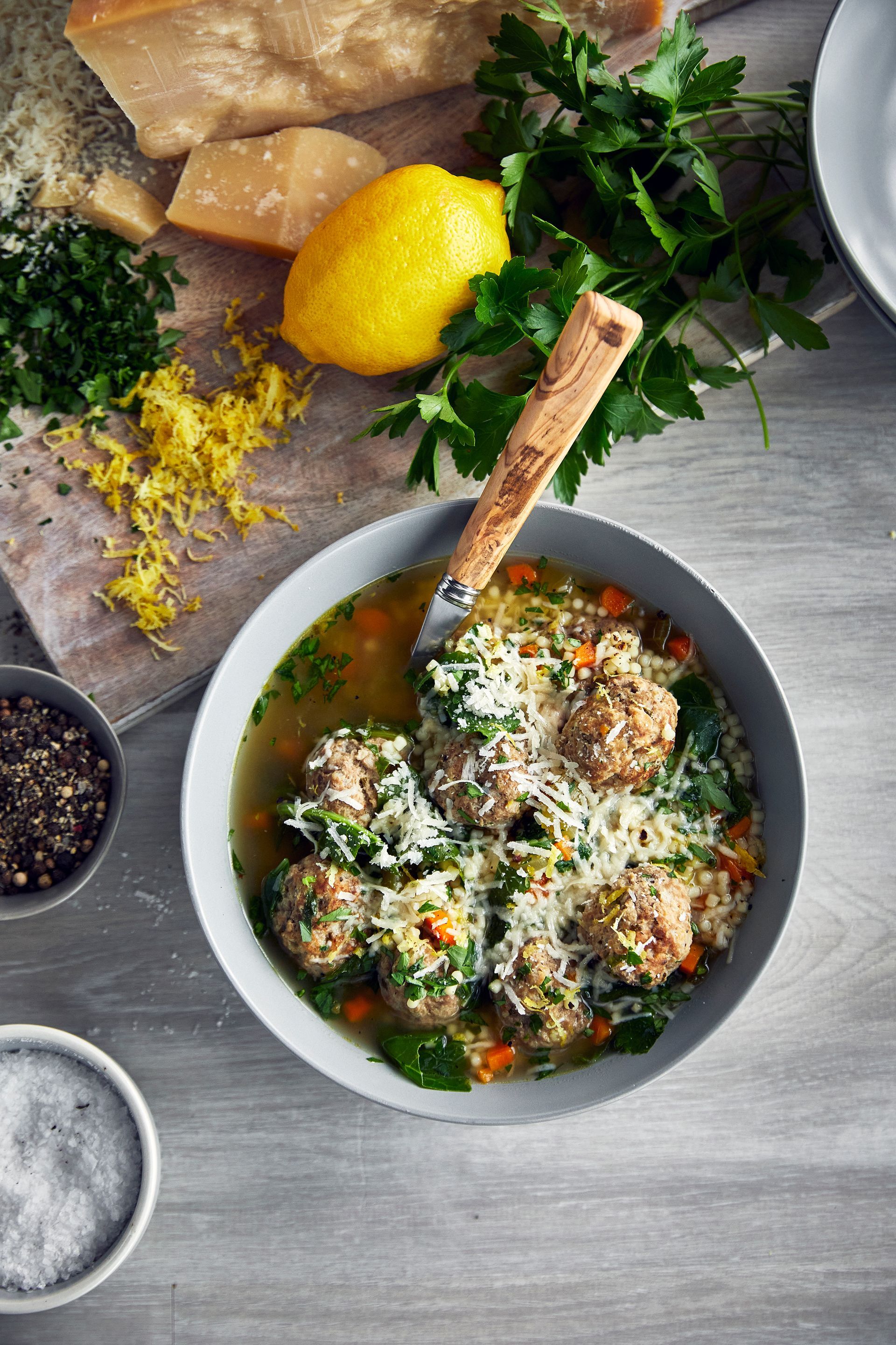 A bowl of Italian wedding soup with meatballs and vegetables on a table.