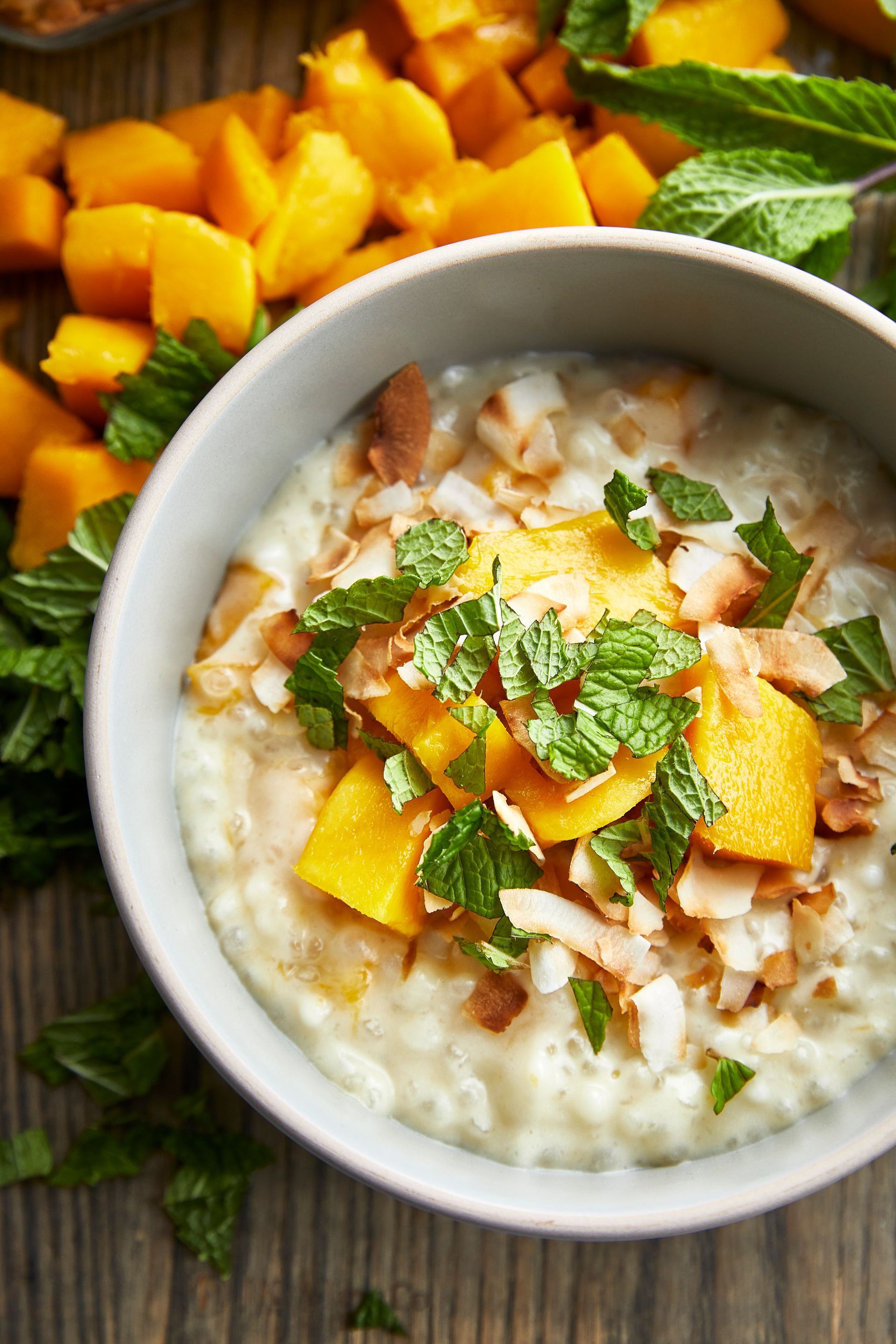 A bowl of rice pudding with mango and mint on a wooden table.
