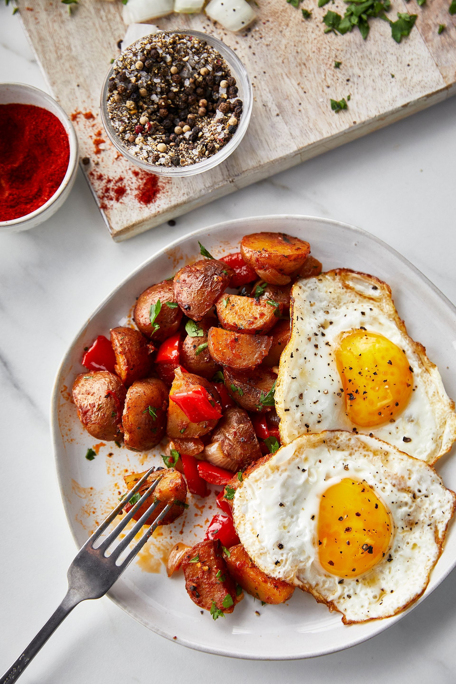 A plate of food with eggs and potatoes on a table with a fork.
