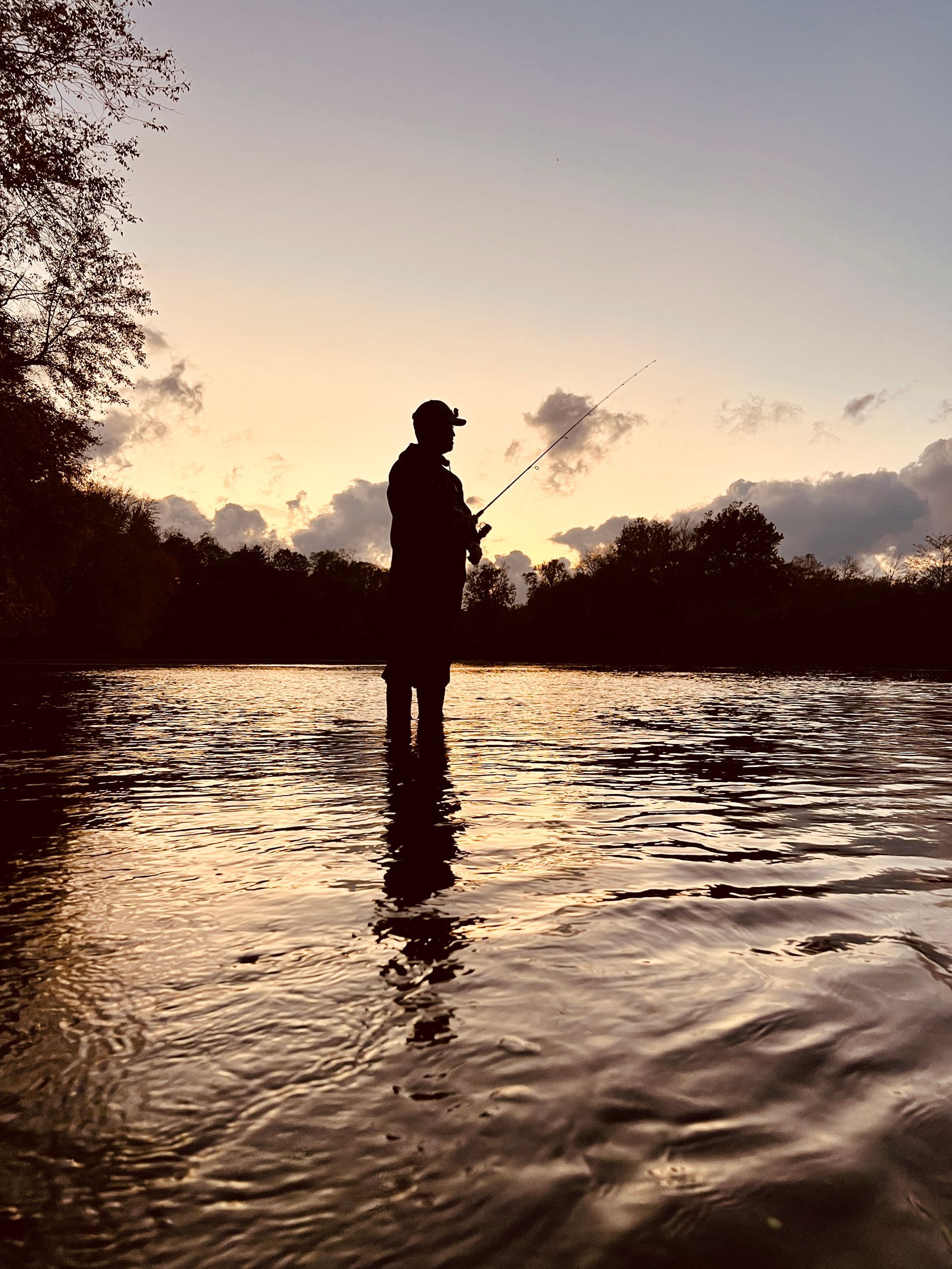 A man is fishing in a river at sunset.