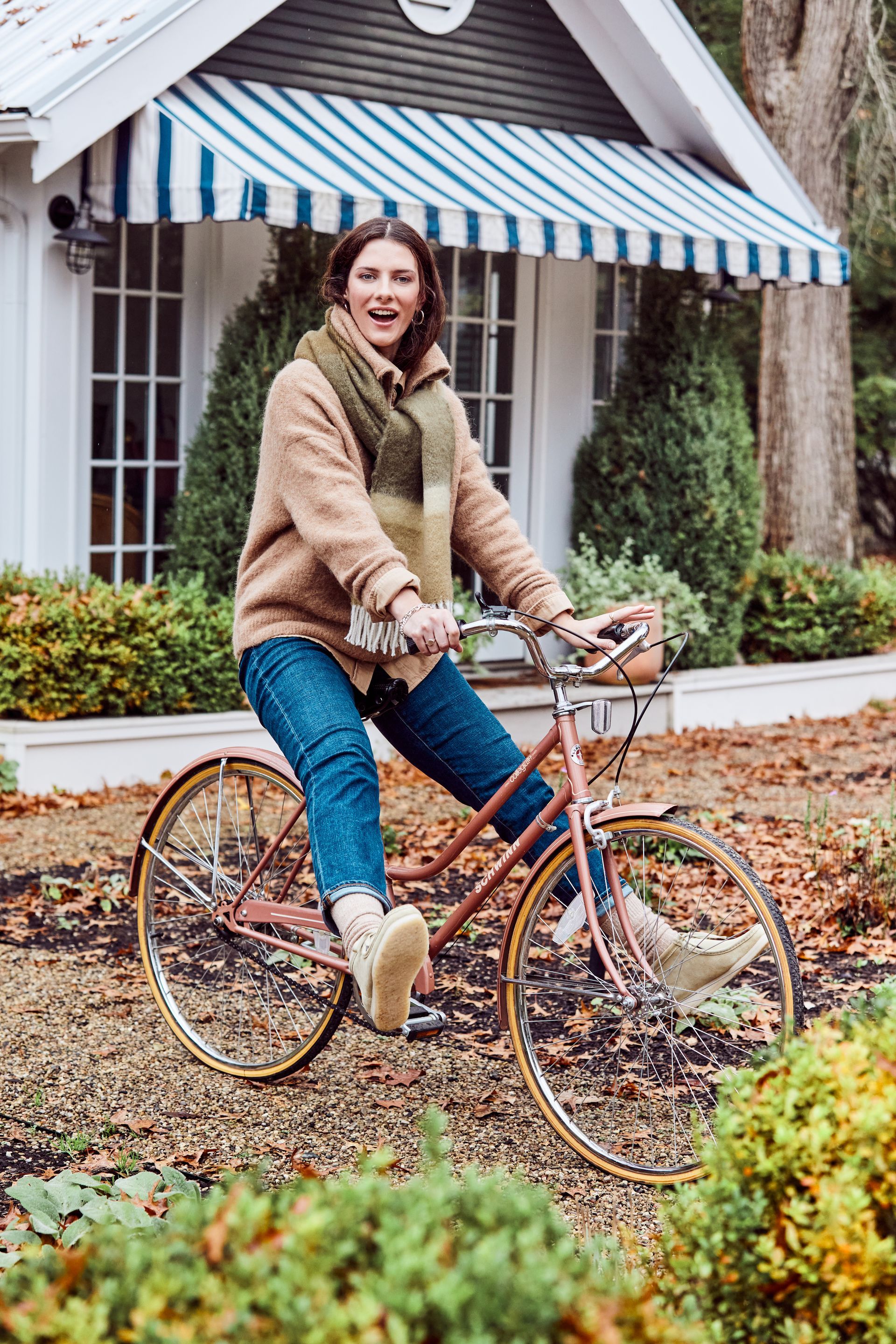 A woman is riding a bicycle in front of a house with a striped awning.