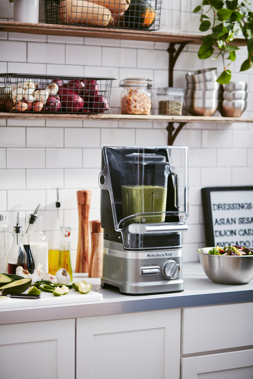 A KitchenAid commercial blender is sitting on a kitchen counter next to a bowl of food.