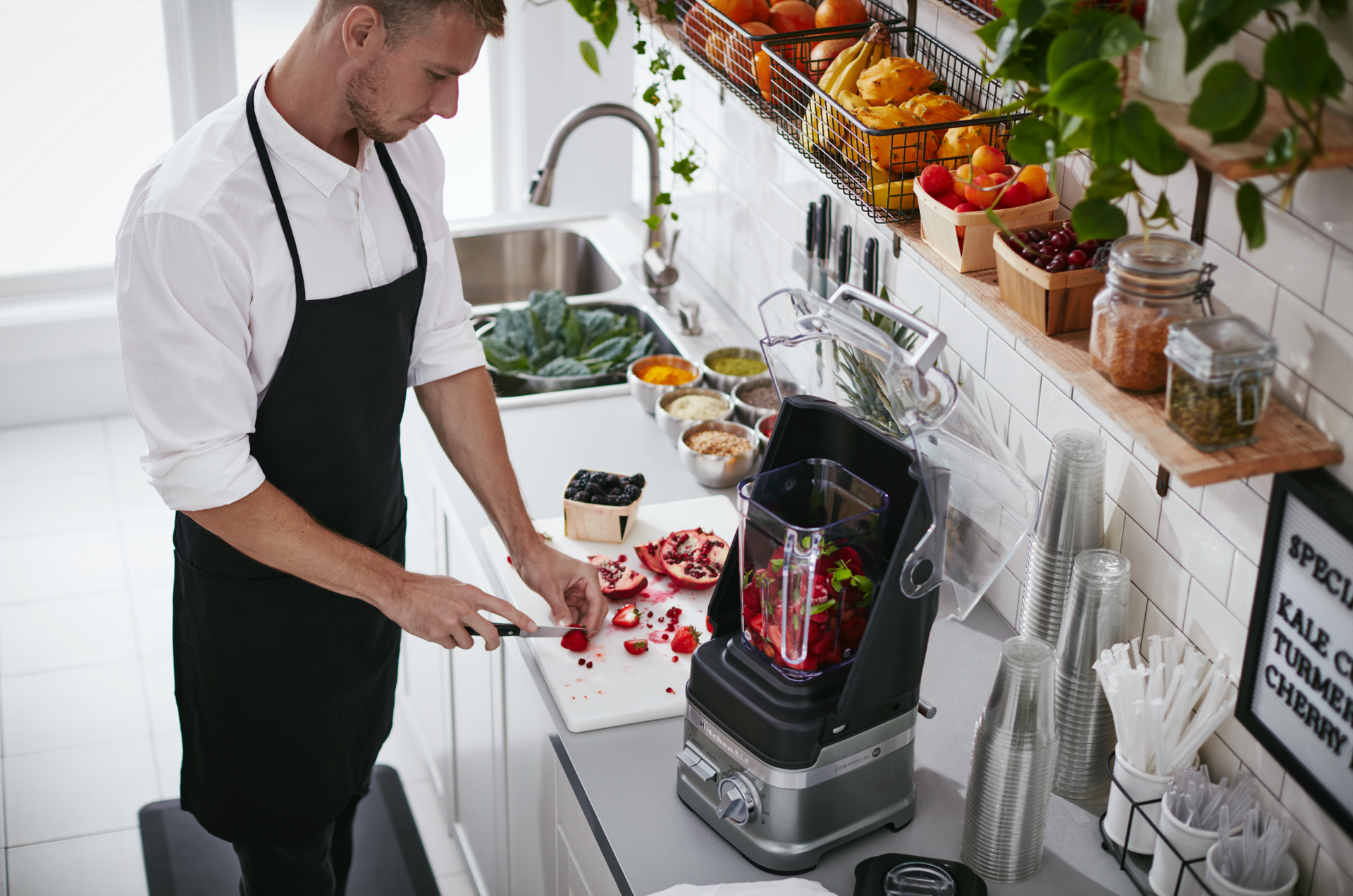 A man is cutting strawberries on a cutting board in a kitchen.