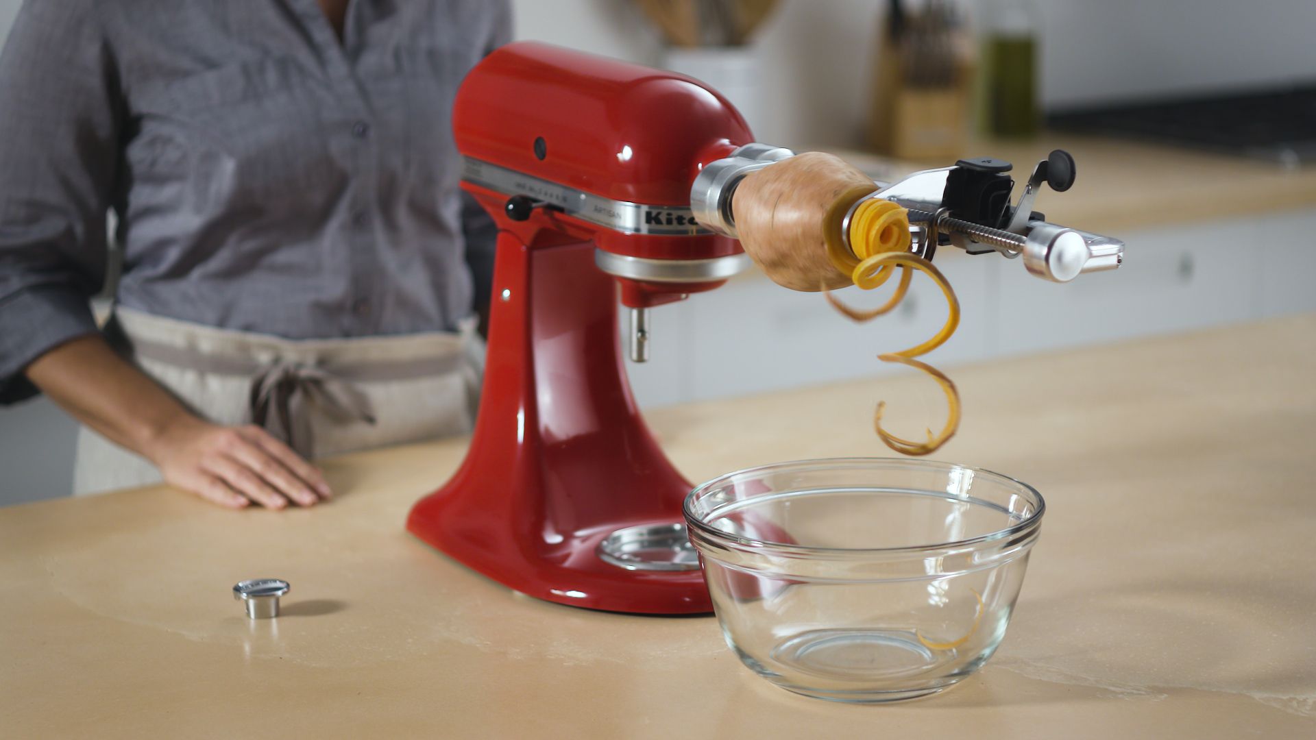 A woman is using a KitchenAid mixer to spiralize an potato.