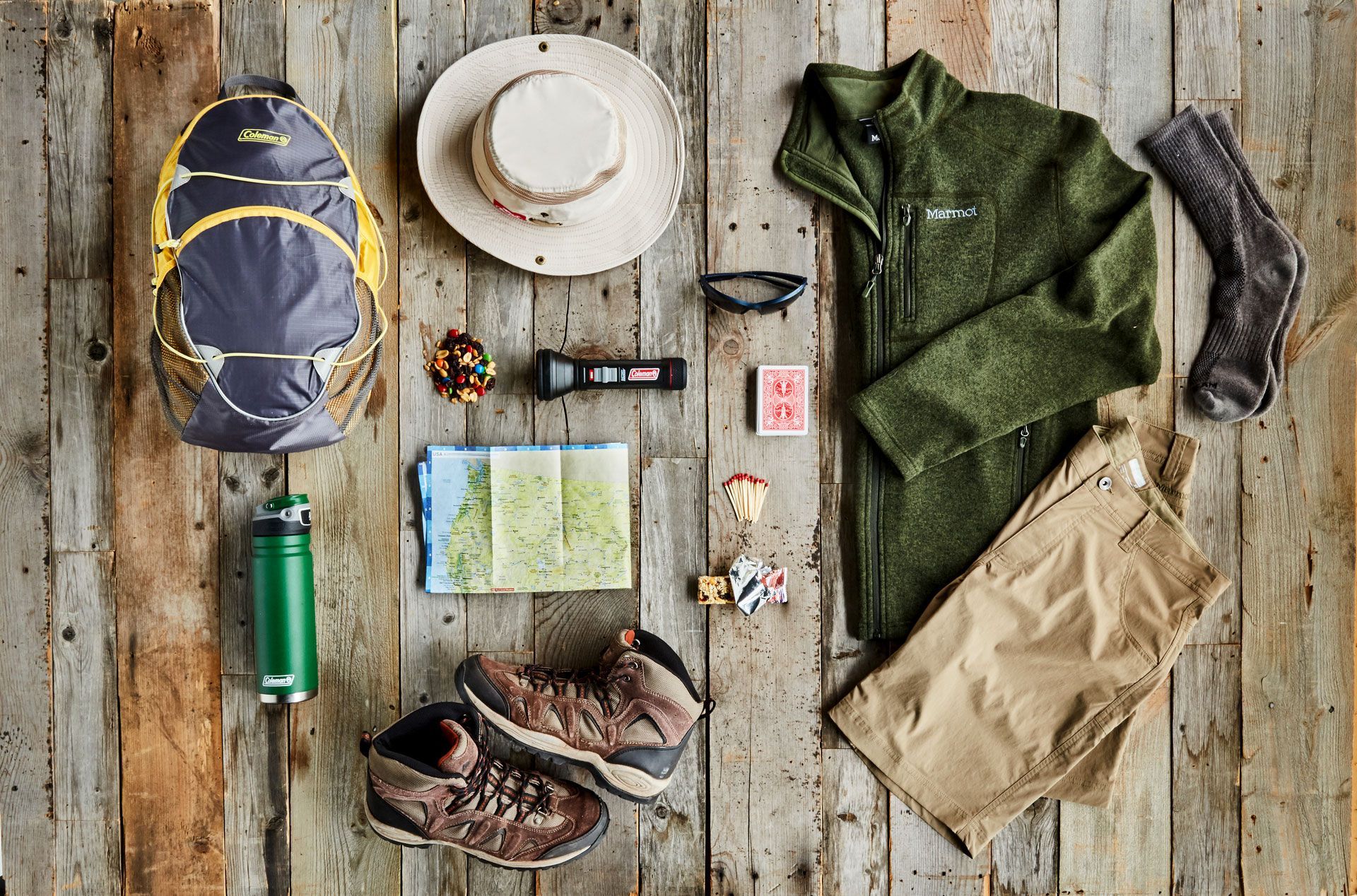 A wooden table topped with hiking gear and a hat.