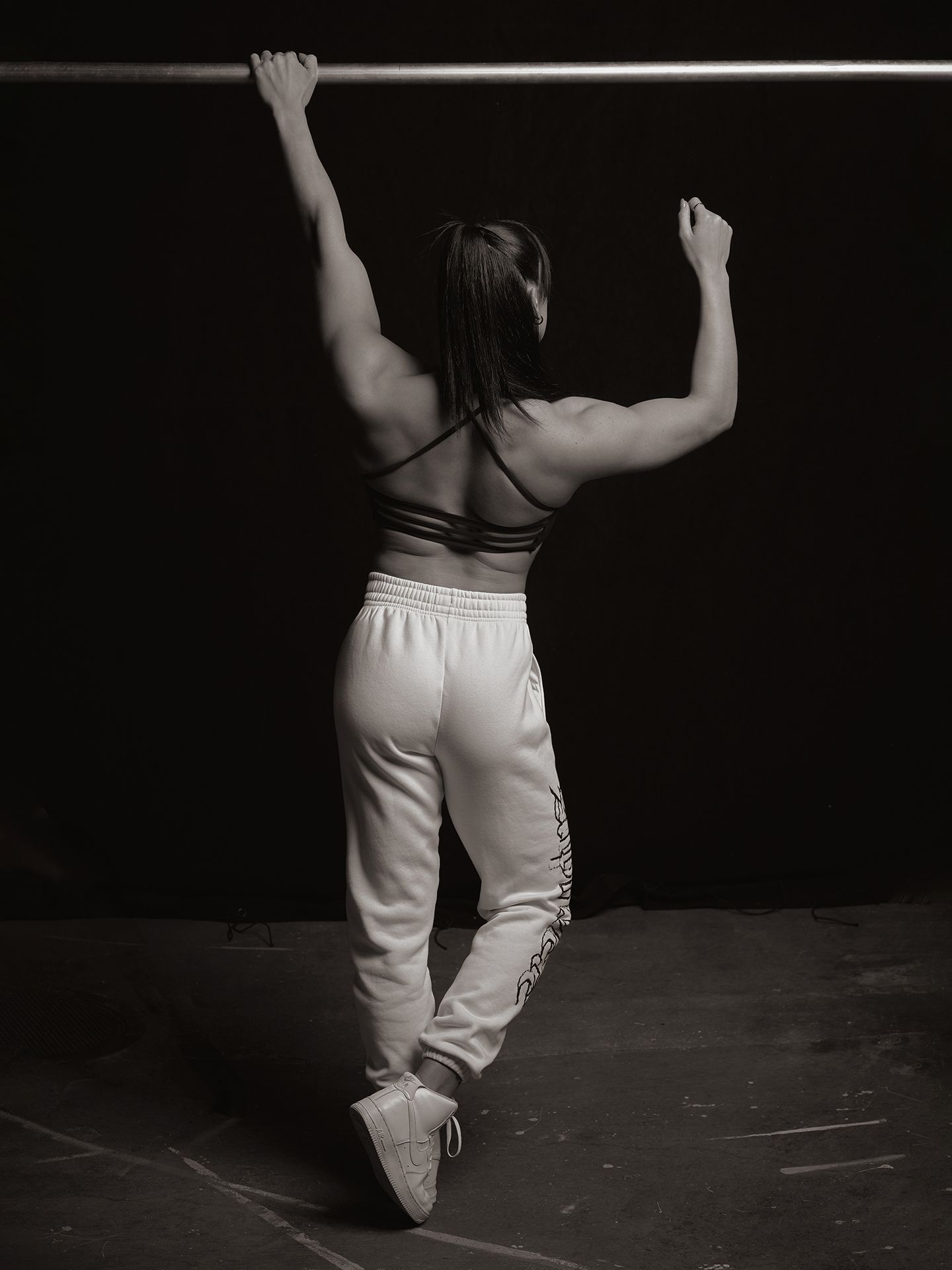 A woman is doing a pull up on a bar in a black and white photo.