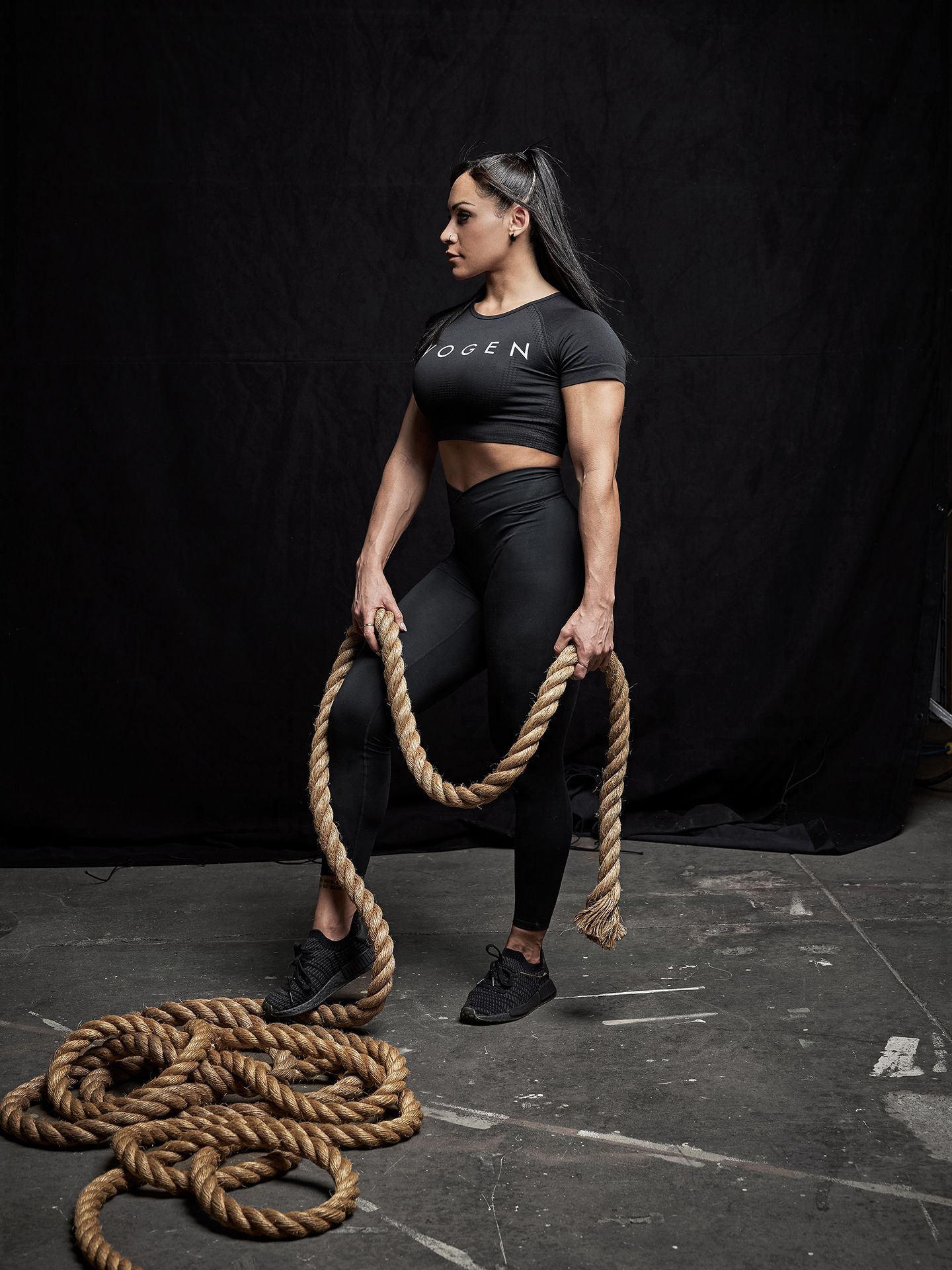 a woman in black workout clothes and a rope is standing in front of a black background