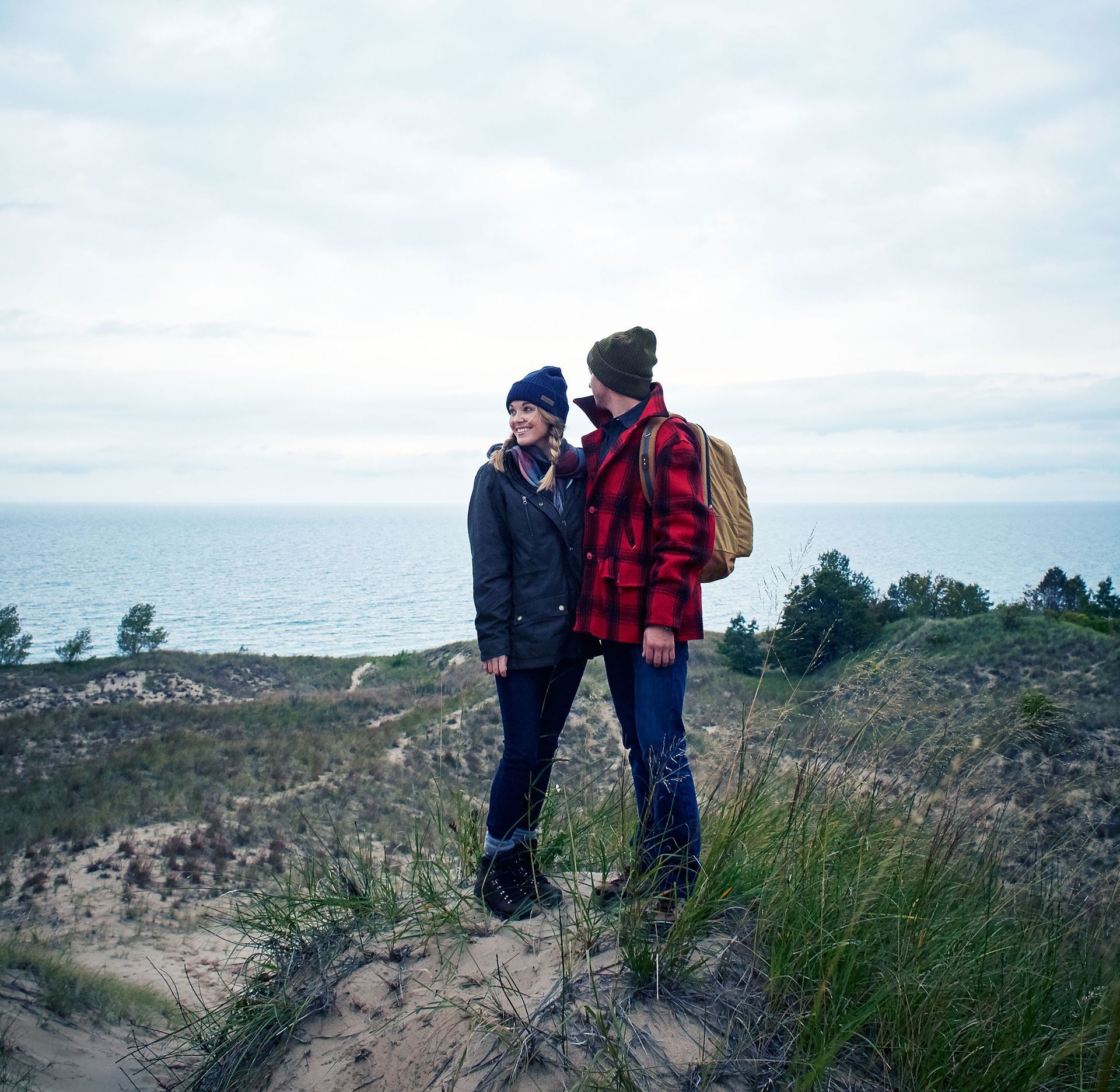 A man and a woman in hiking clothes standing next to each other on a hill overlooking the Lake Michigan