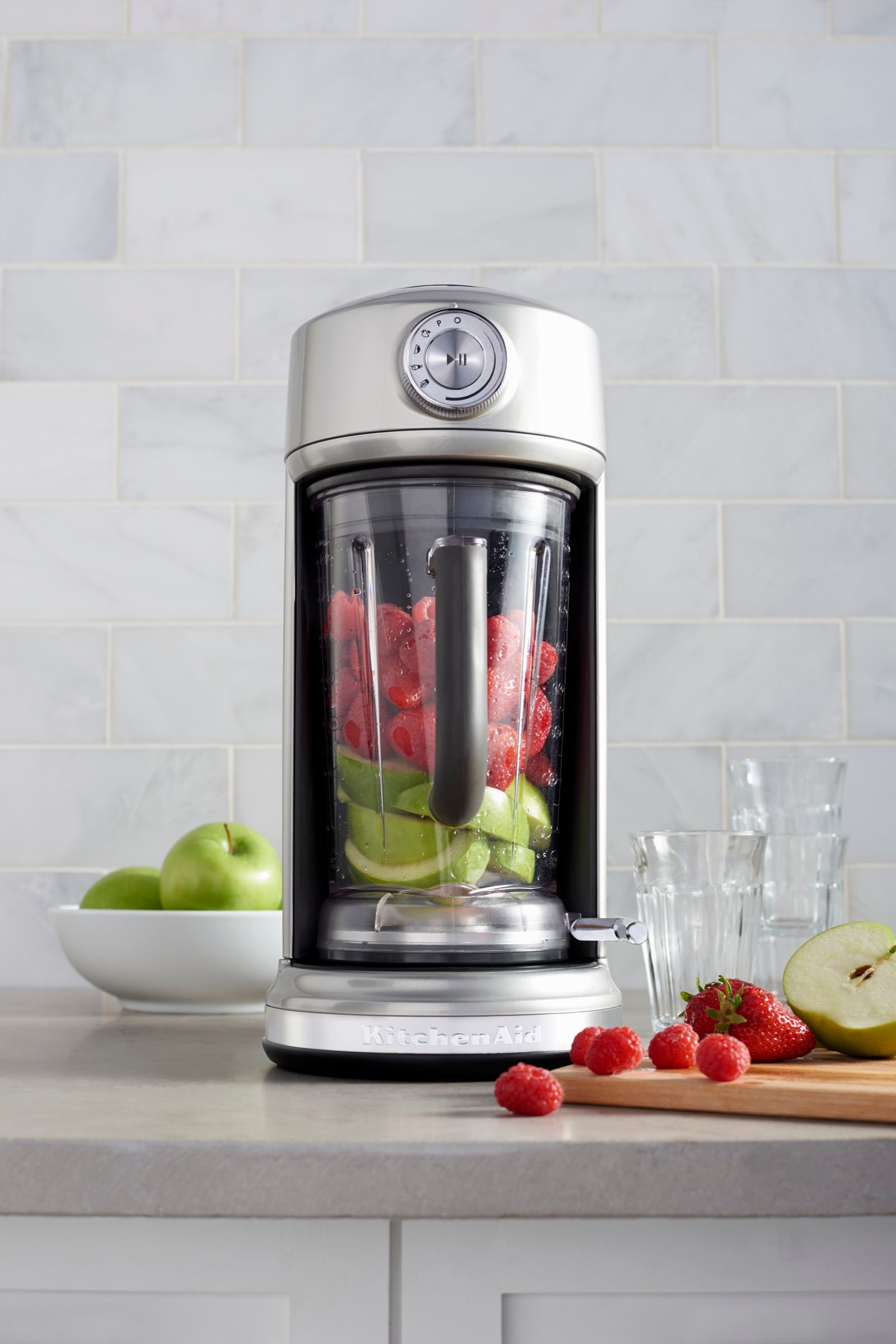 A KitchenAid blender is filled with fruit on a counter.