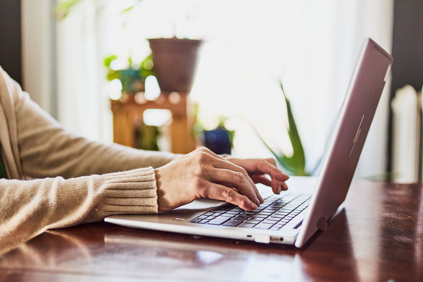 A person is typing on a laptop computer on a wooden table.