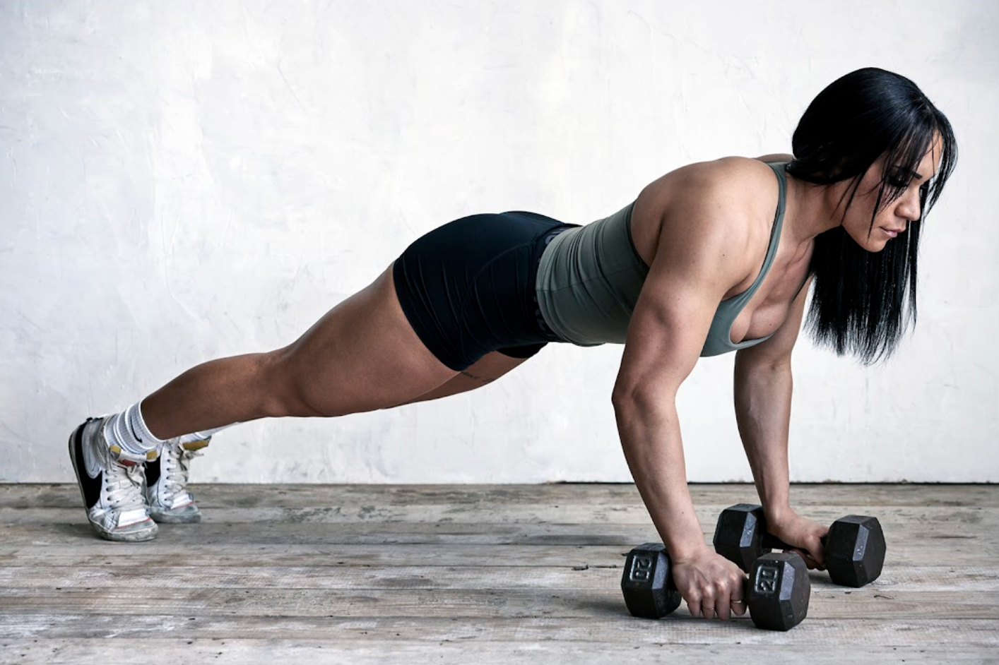 A woman is doing push ups with dumbbells on the floor.