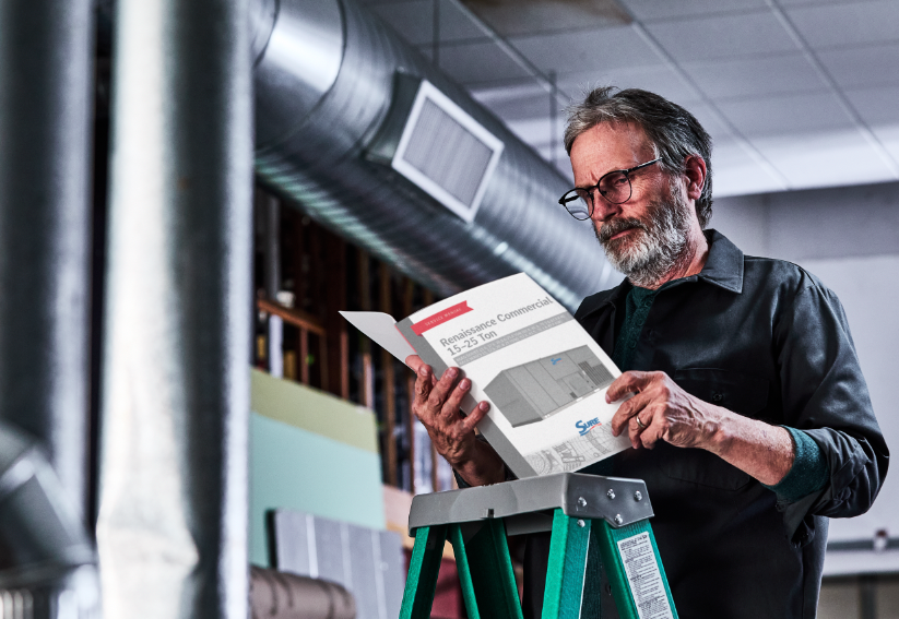 A man is standing on a ladder reading a service manual