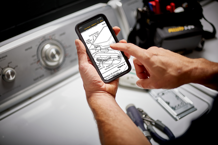 A person is holding a cell phone in front of a washing machine.