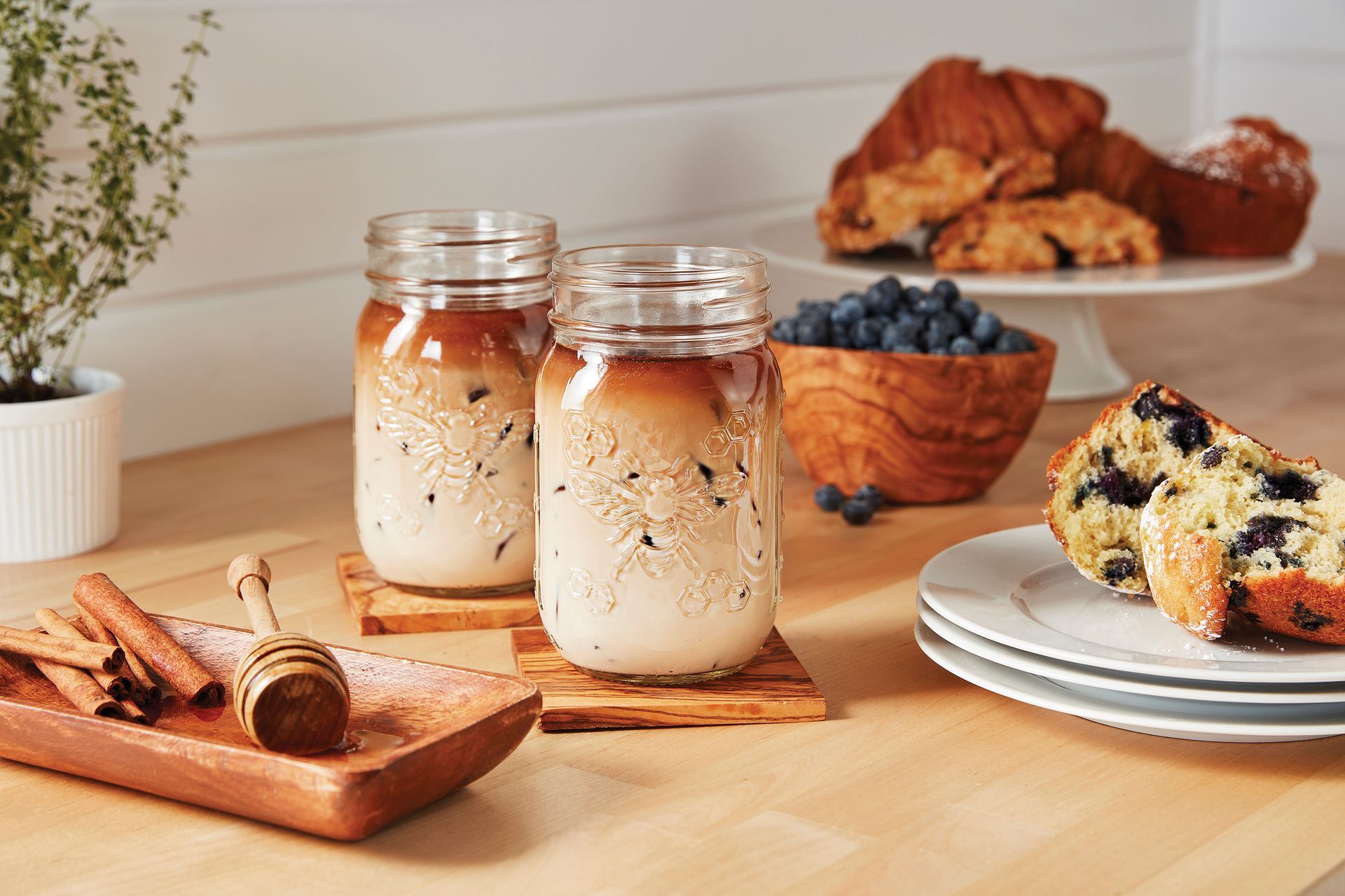 A wooden table topped with Ball jars filled with iced coffee and muffins on a plate