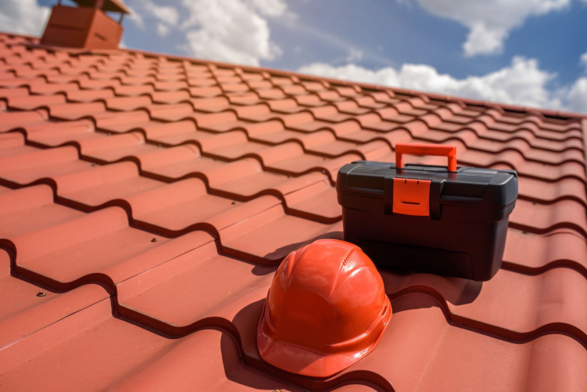 A hard hat and a toolbox are sitting on top of a red tiled roof.
