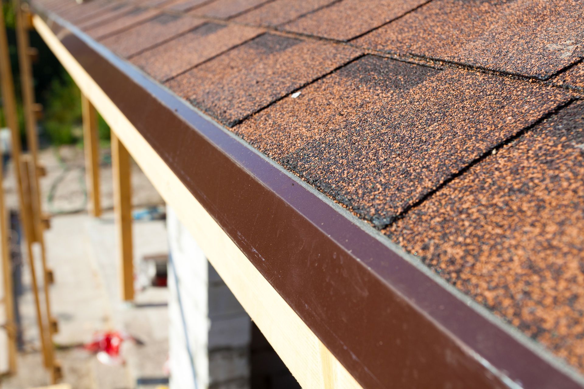 A close up of a roof with shingles and a brown gutter.