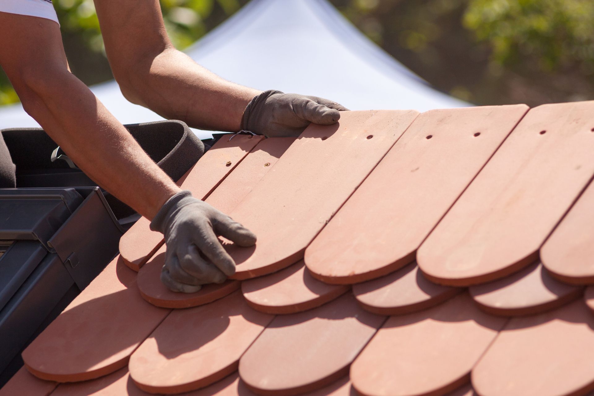 A man is working on a roof with red tiles.