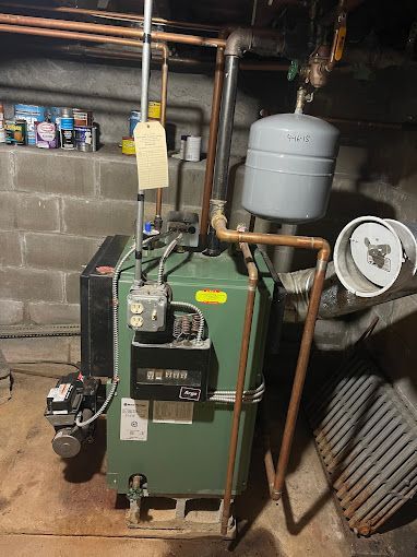 A green boiler is sitting in a basement next to a brick wall.