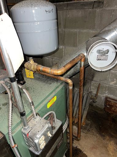 A green boiler with copper pipes attached to it in a basement.