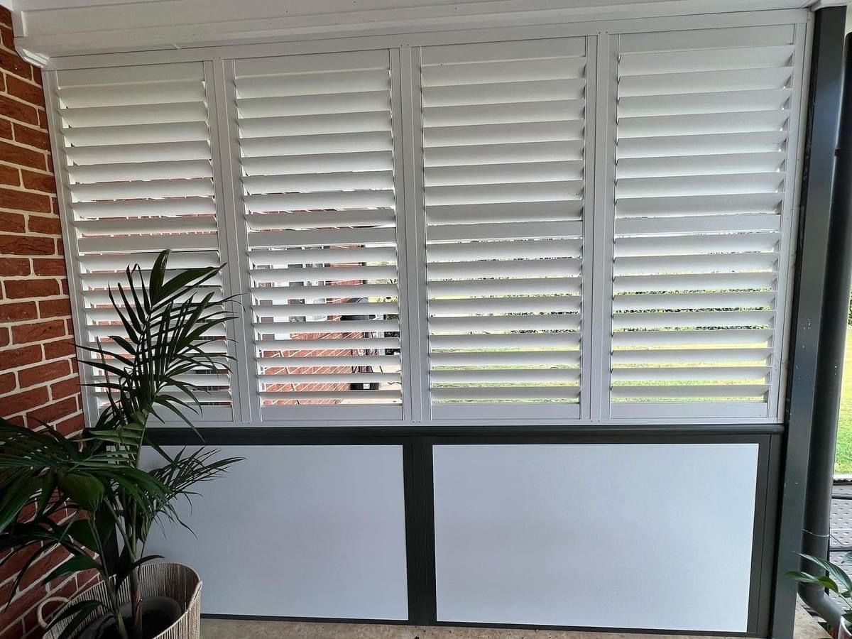 A room with a brick wall and white shutters on the windows.