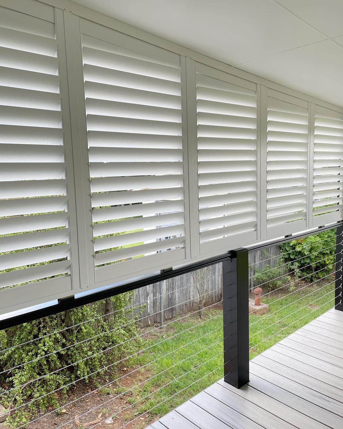 A balcony with white shutters on the windows and a black railing.