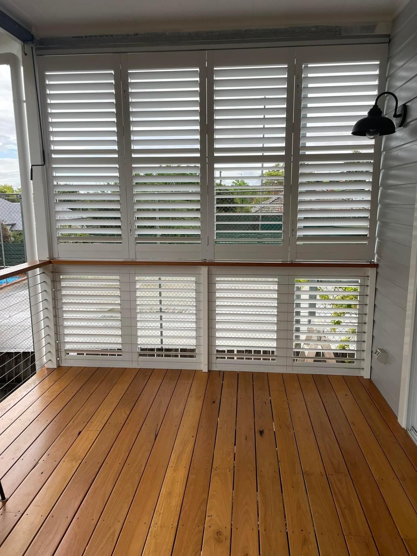 A room with a wooden floor and white shutters on the windows.