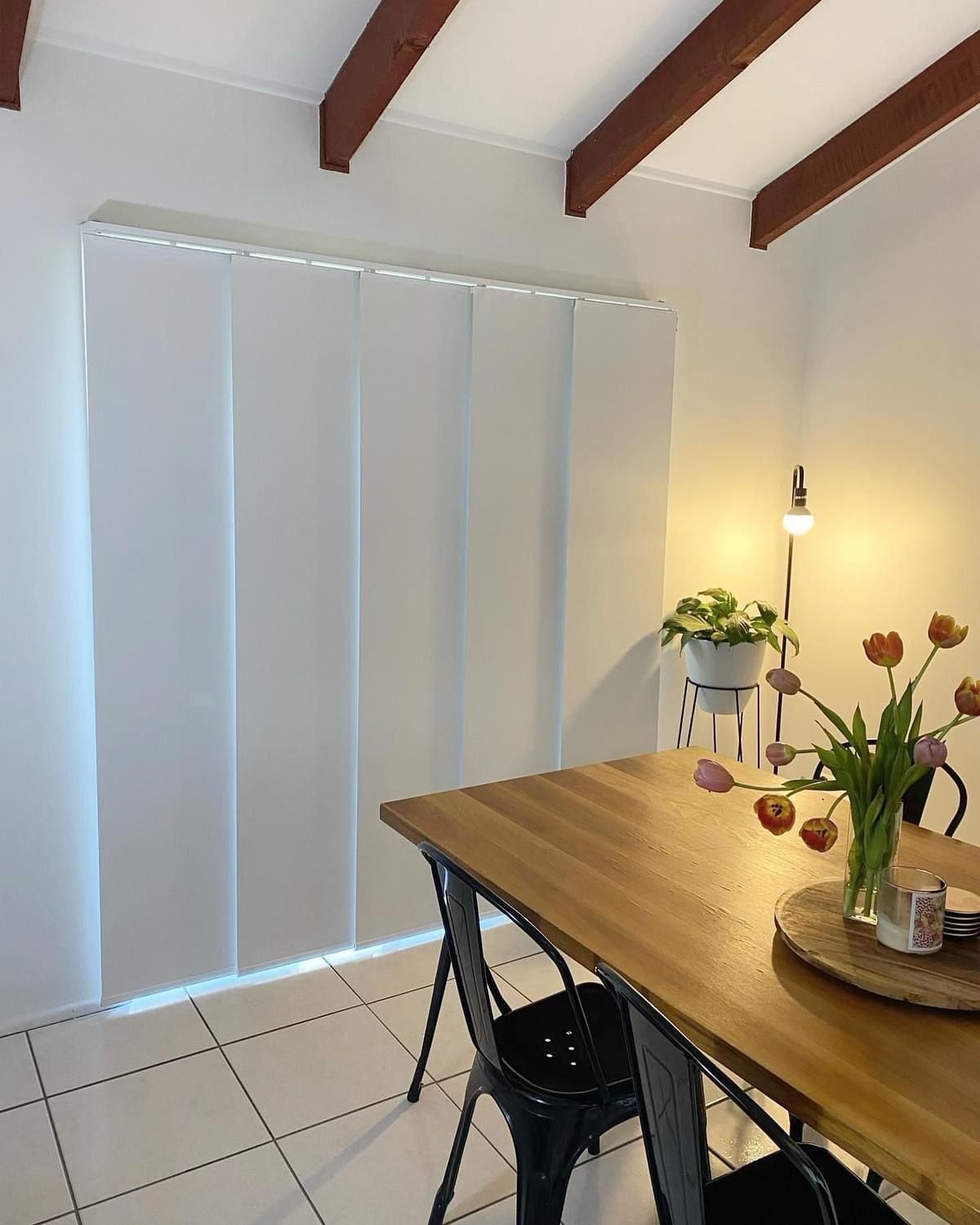 A dining room with a wooden table and chairs and a vase of flowers on the table.