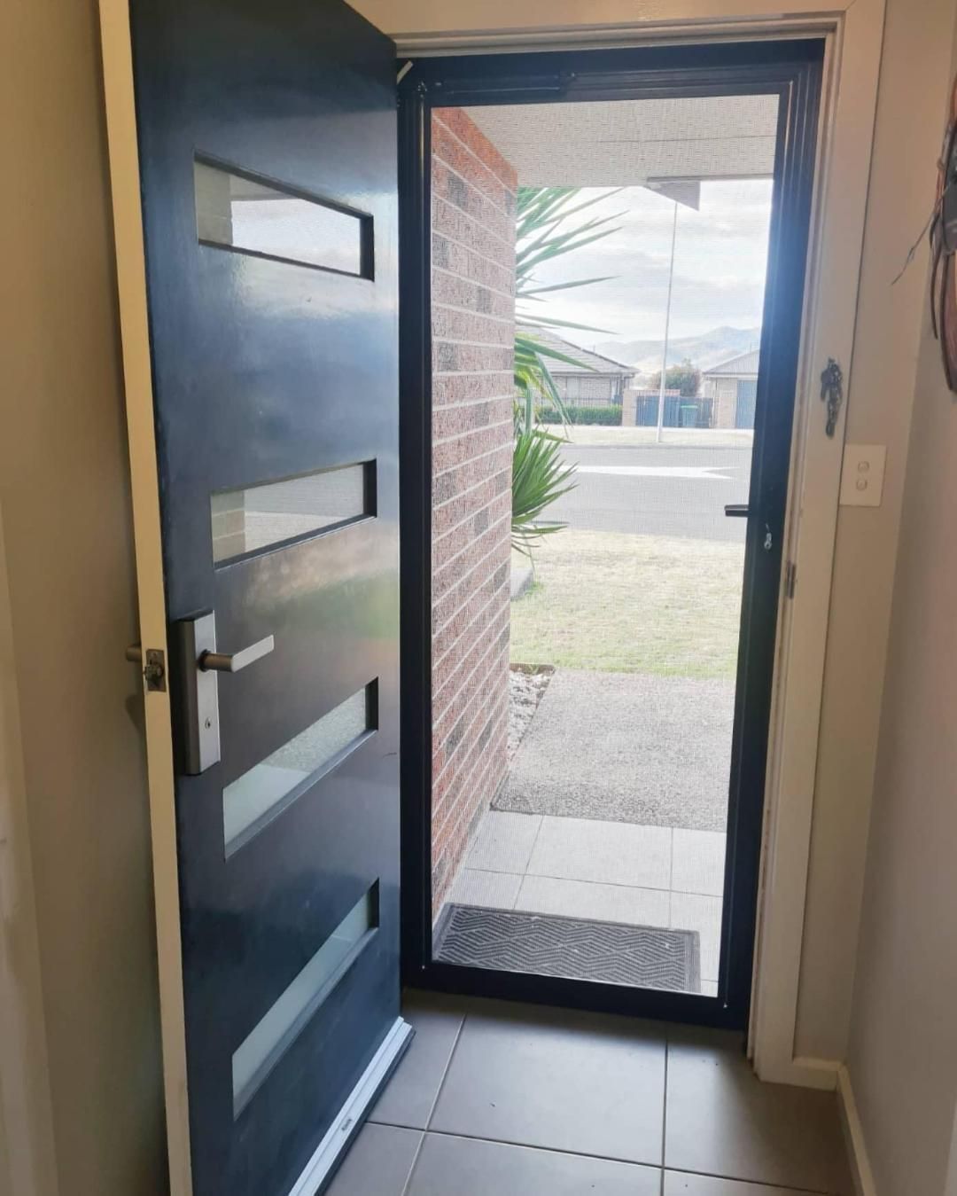 A black door with a glass window is open to a brick wall.