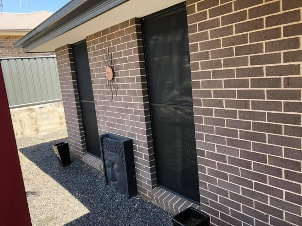 A brick house with a black screen door and two windows.