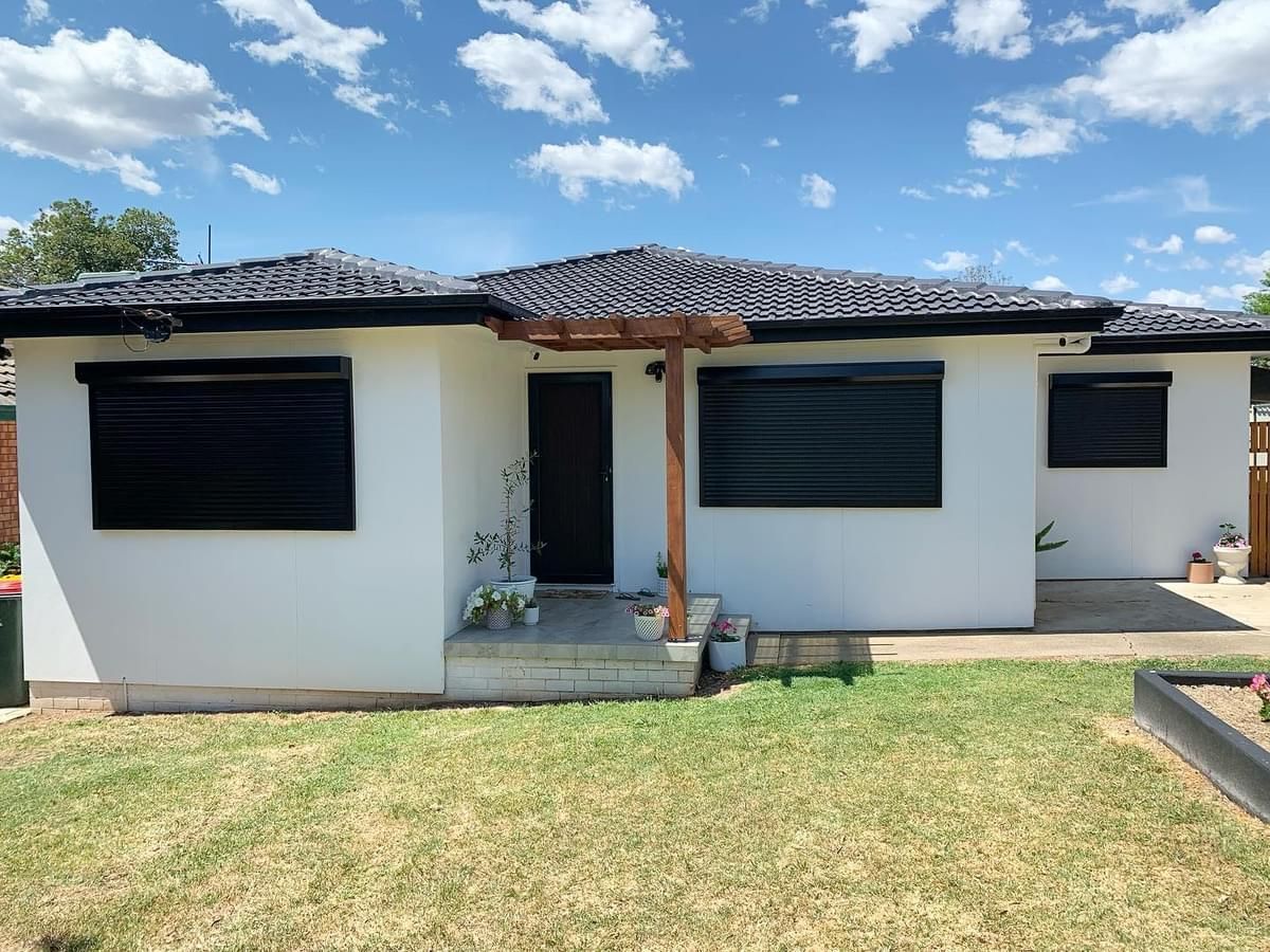 A white house with black shutters on the windows is sitting on top of a lush green lawn.
