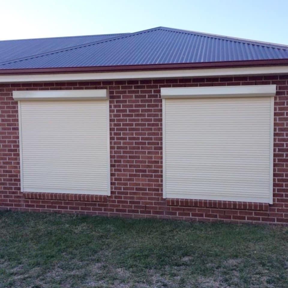 A brick house with two white roller shutters on the windows.