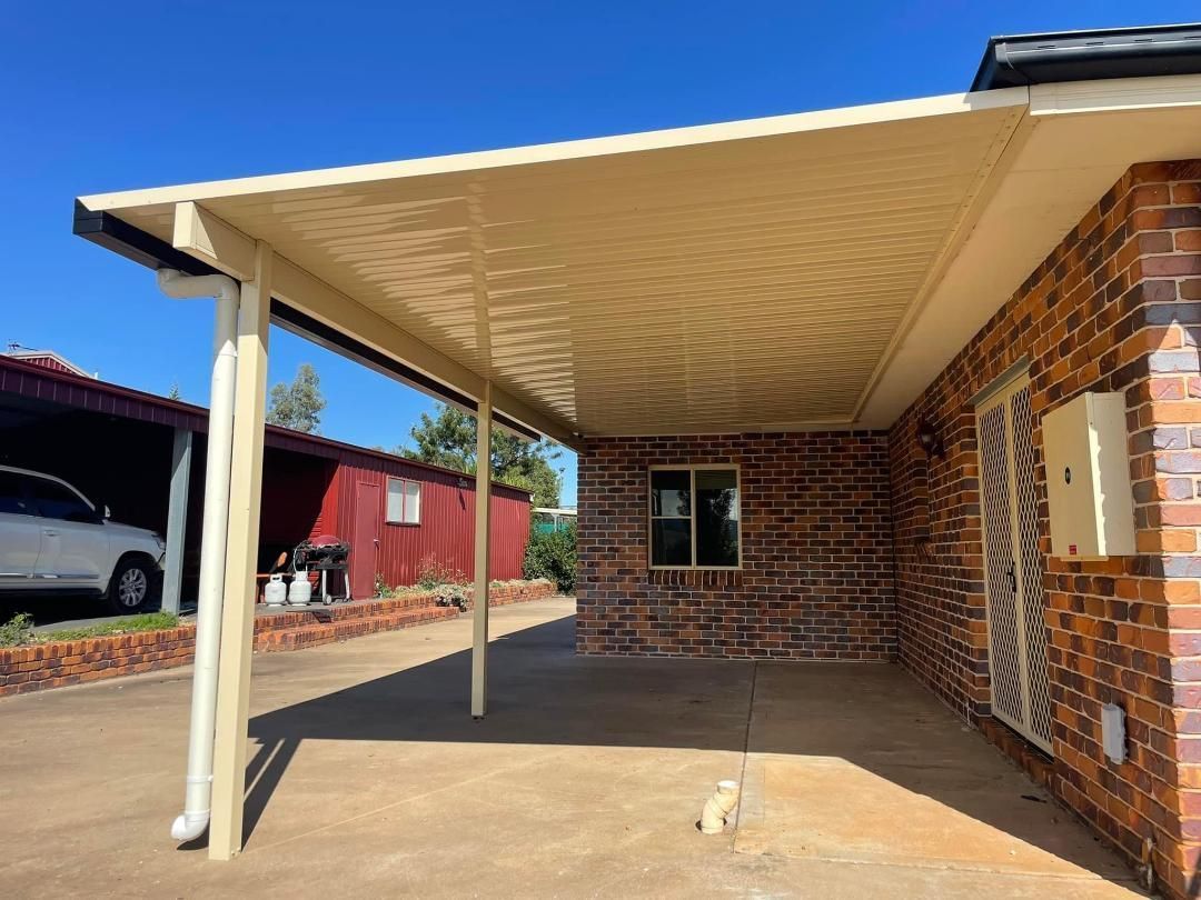 A car is parked under a covered porch in front of a brick house.