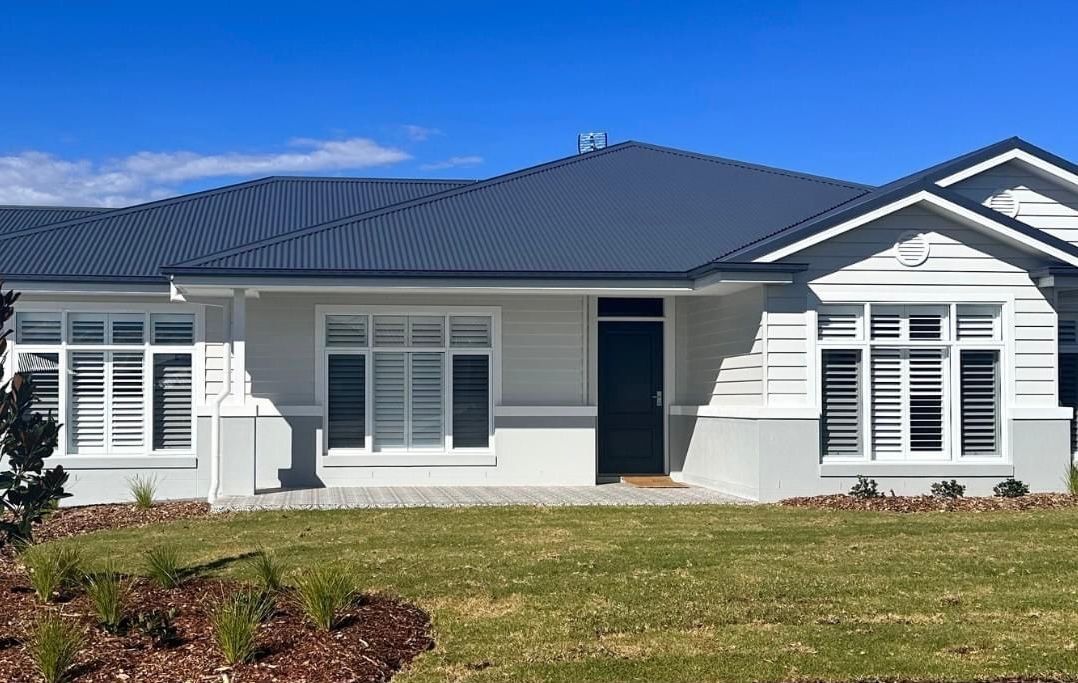 A white house with a black roof is sitting on top of a lush green field.