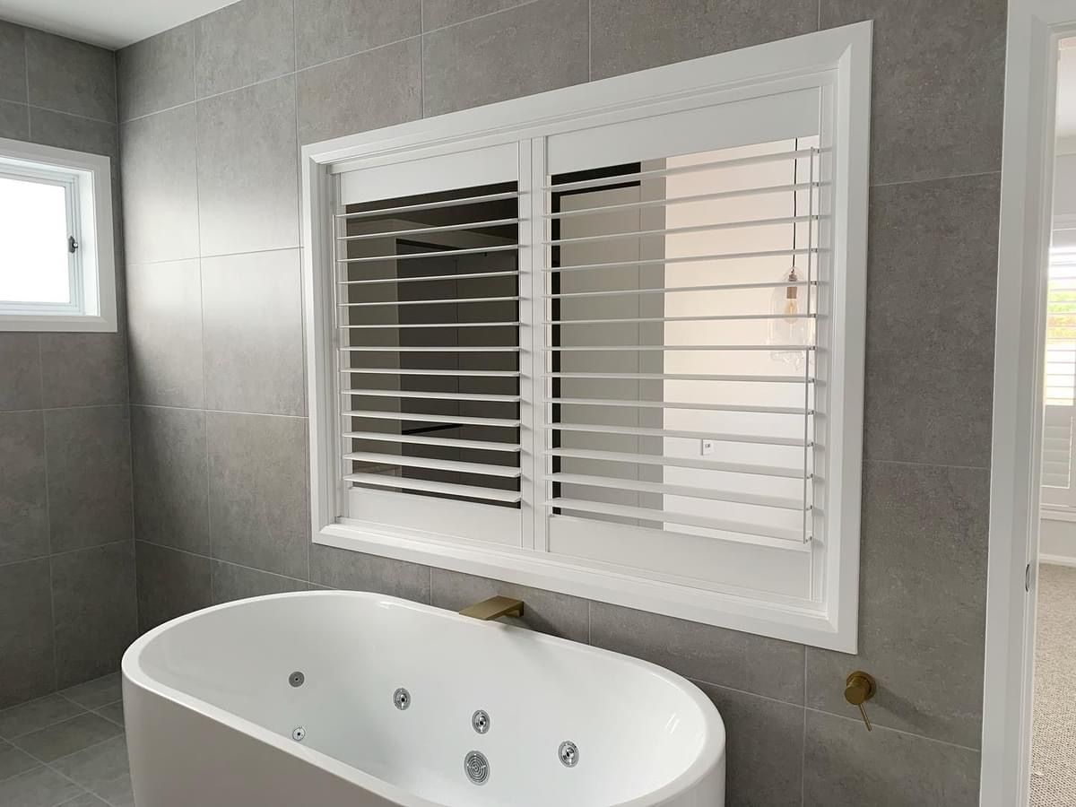 A bathroom with a bathtub and a window with shutters.