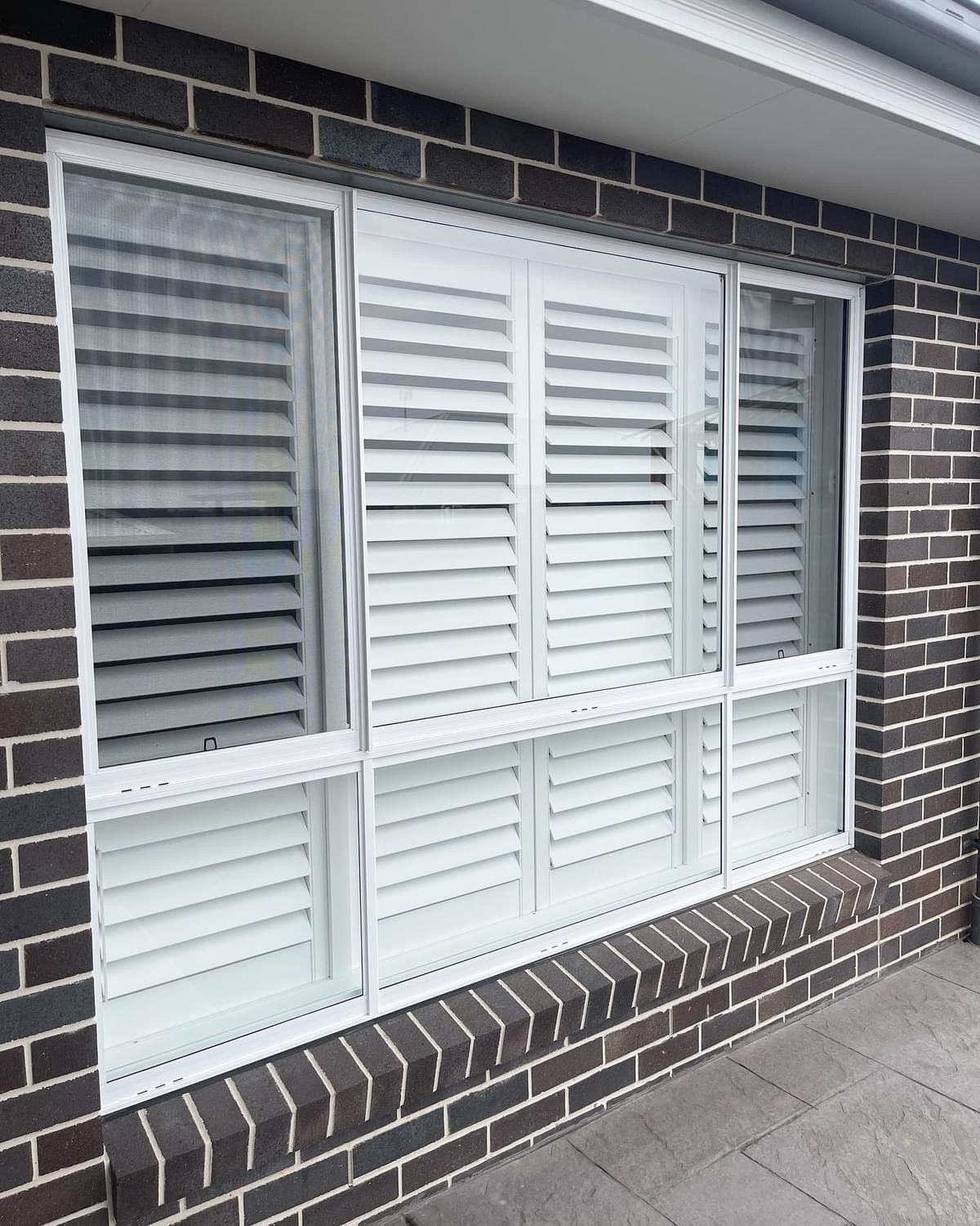 A large window with white shutters on a brick wall.