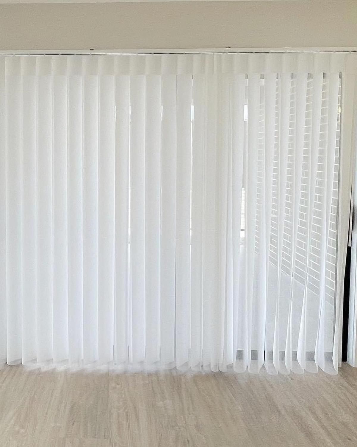 A room with a sliding glass door and white vertical blinds on it.