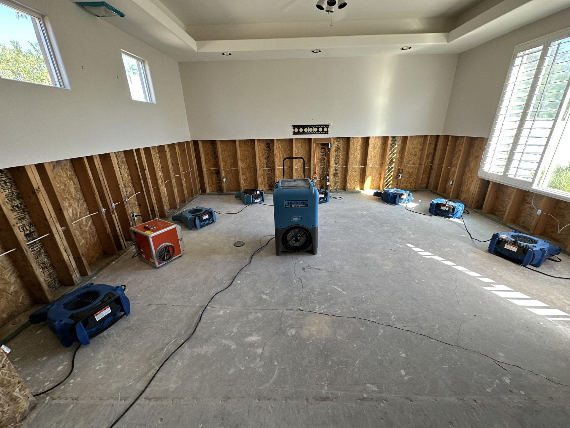 A room with exposed studs and multiple dehumidifiers, likely due to water damage, near windows.