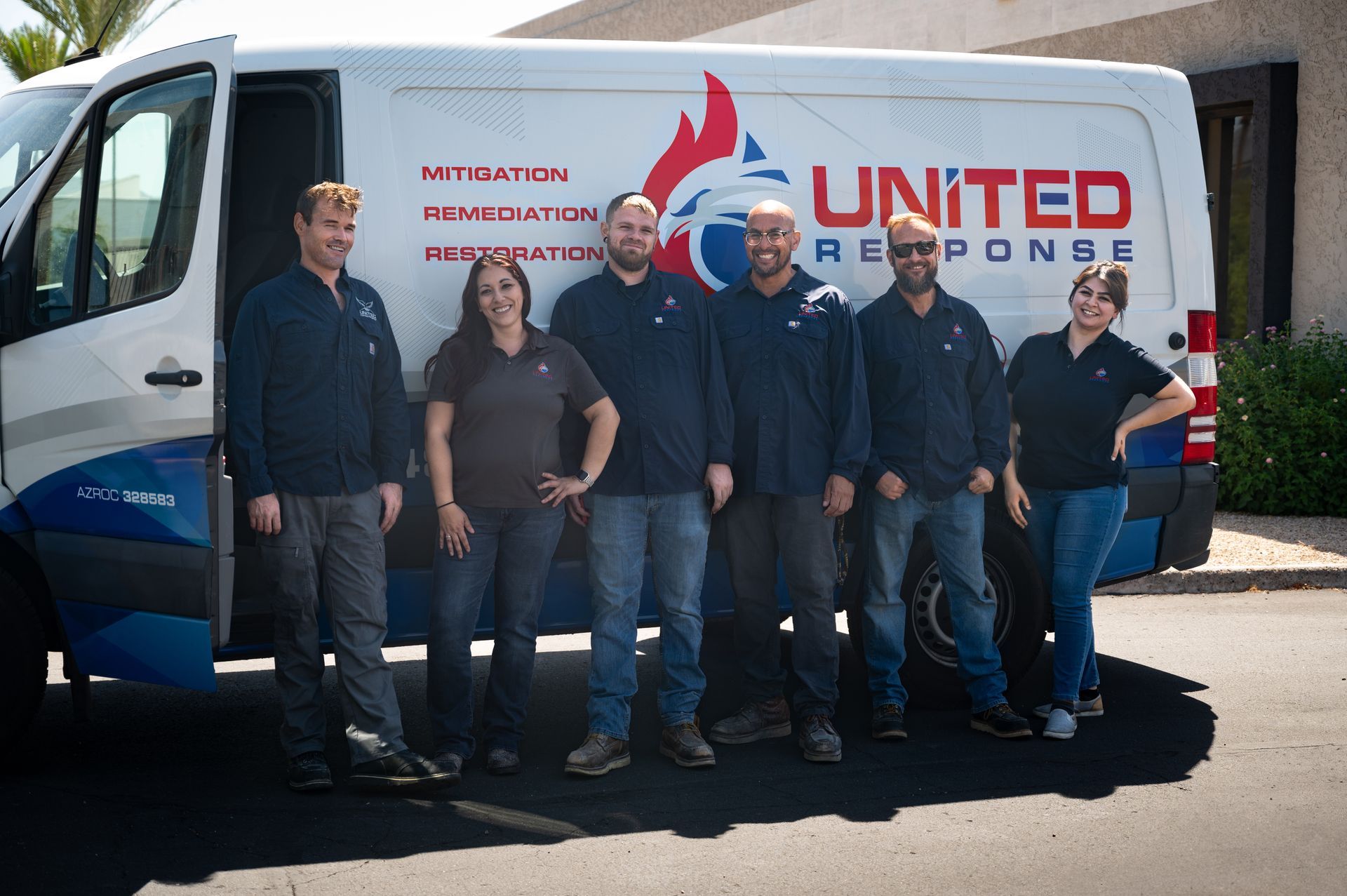 A group of seven people in uniform stand in front of a white van with the logo