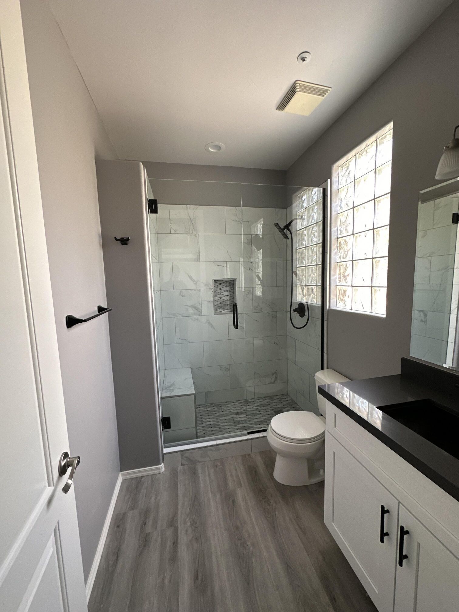 Modern bathroom with gray walls, a glass shower, white vanity, and wood-look flooring.