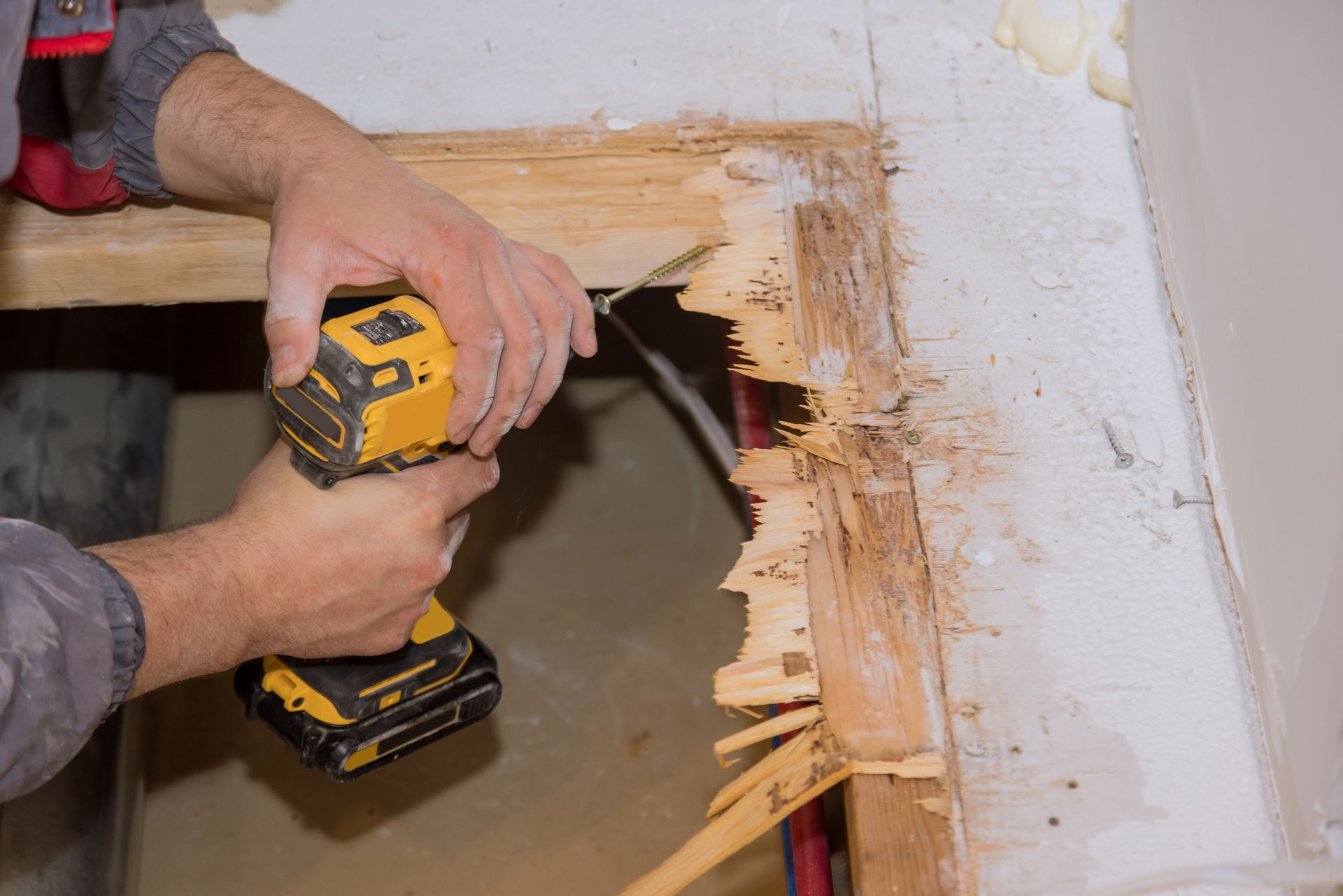 Man using a yellow drill on damaged wood frame.