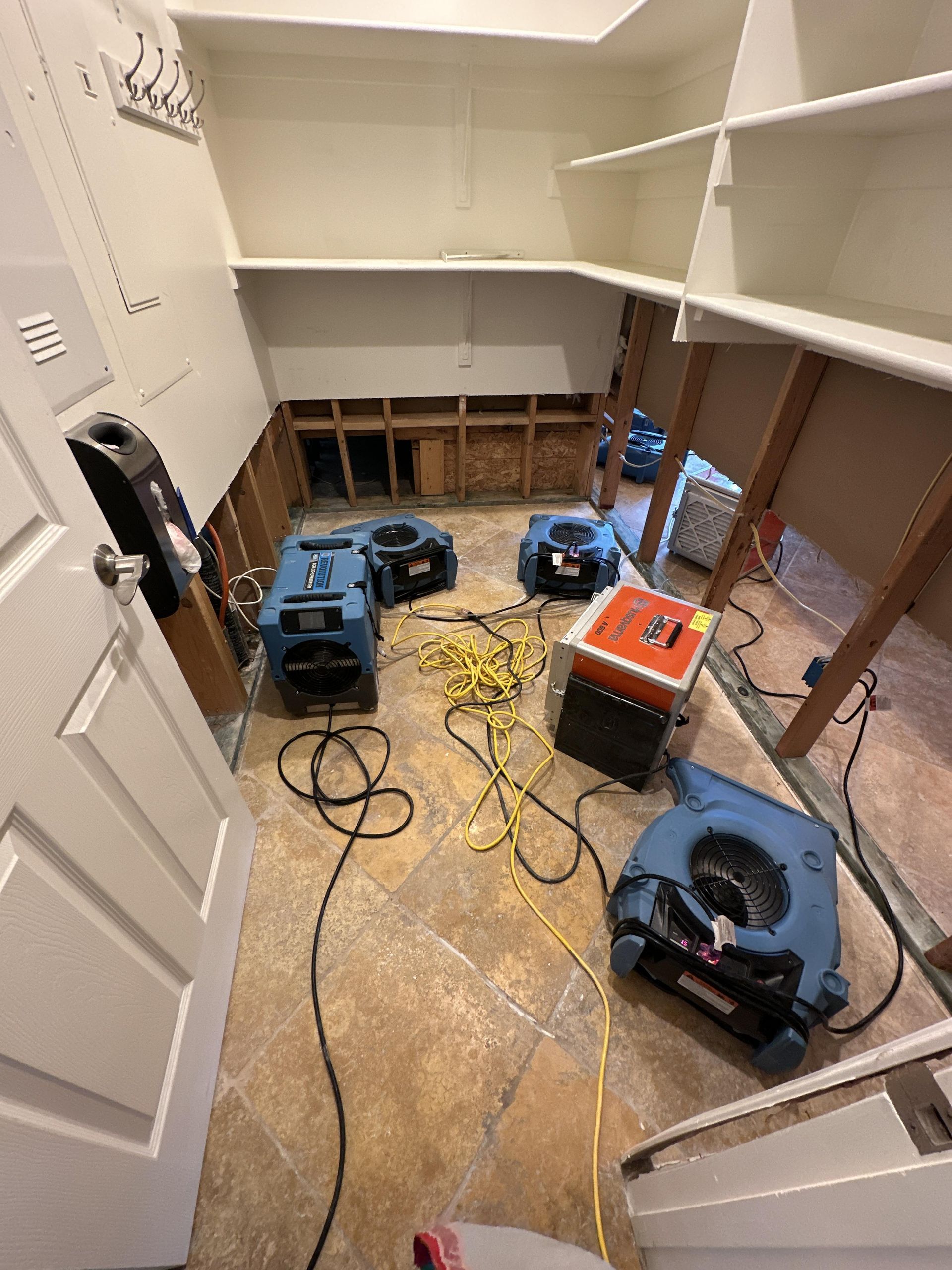 A flooded room with drying equipment. Exposed walls, tile floor, shelving, and a door.