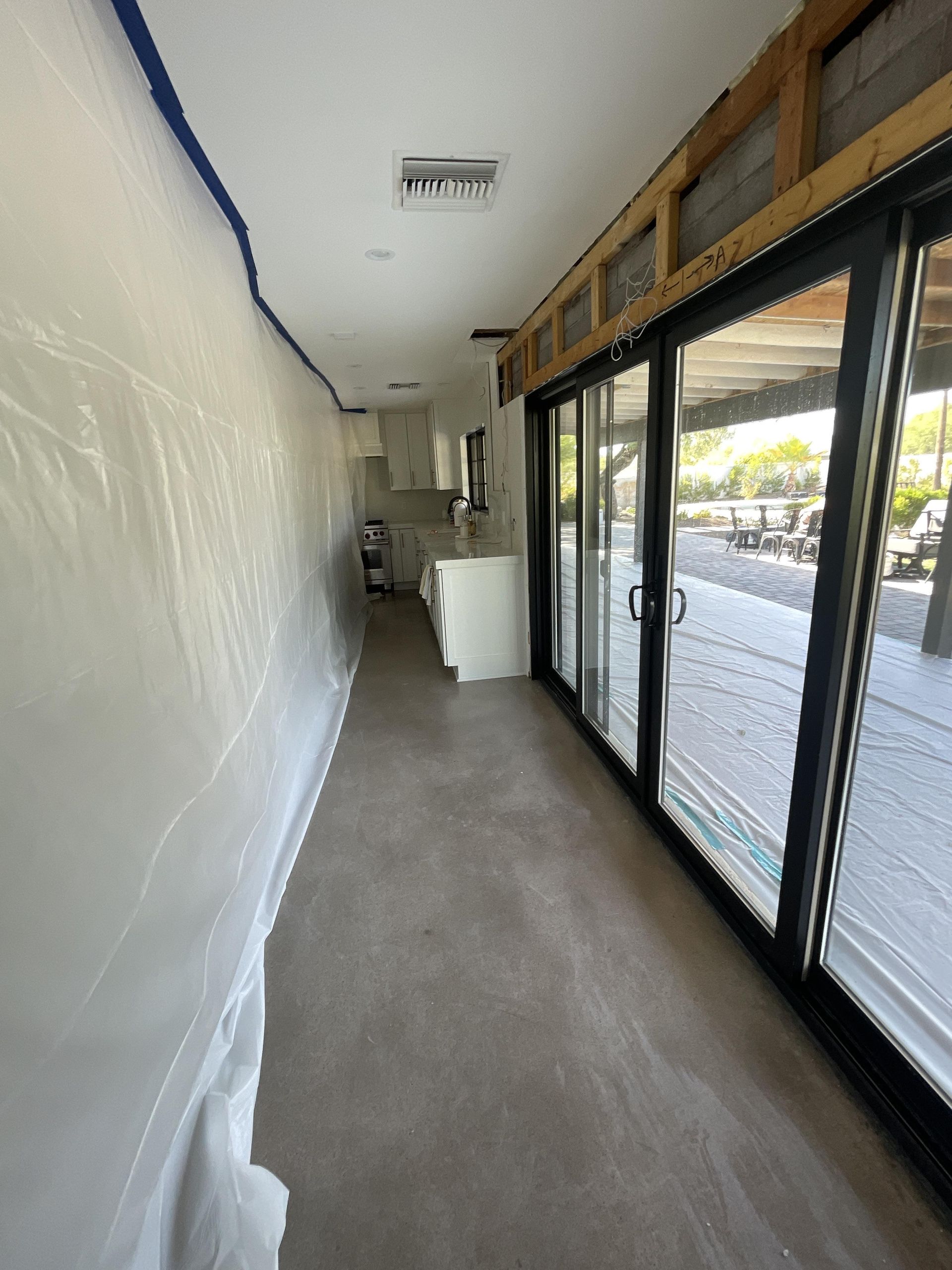 Interior view of a construction zone with plastic sheeting, sliding glass doors, and a kitchen area.