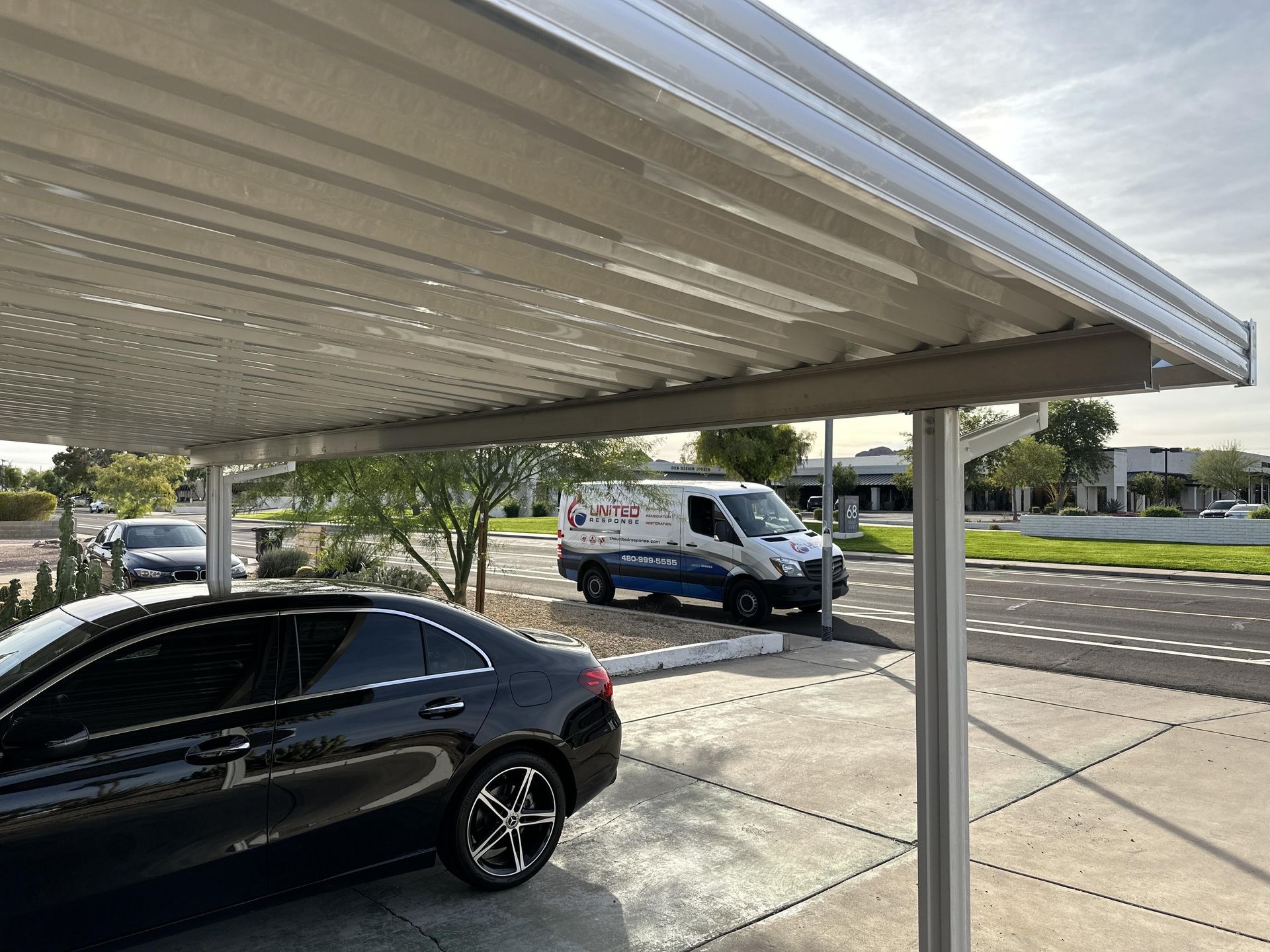 A car parked under a metal carport with a van in the background.