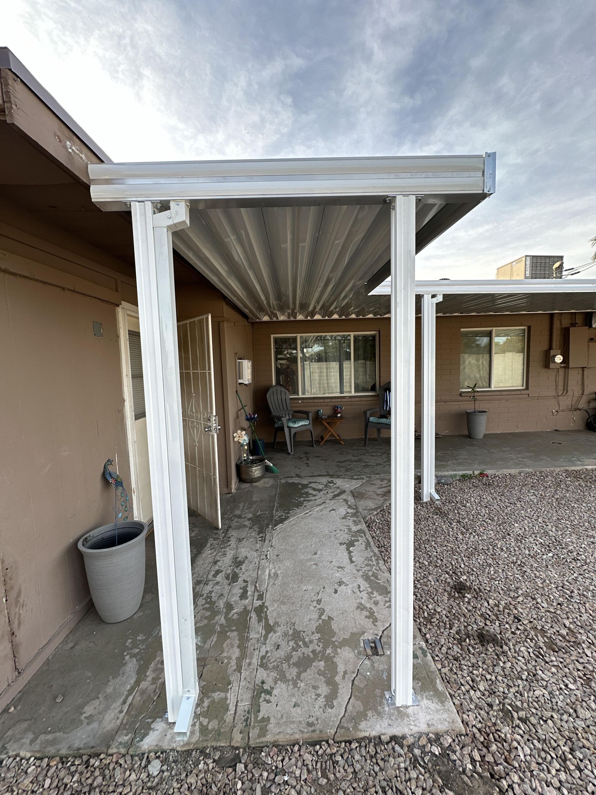 Covered patio attached to a stucco building. White support columns and corrugated metal roof.