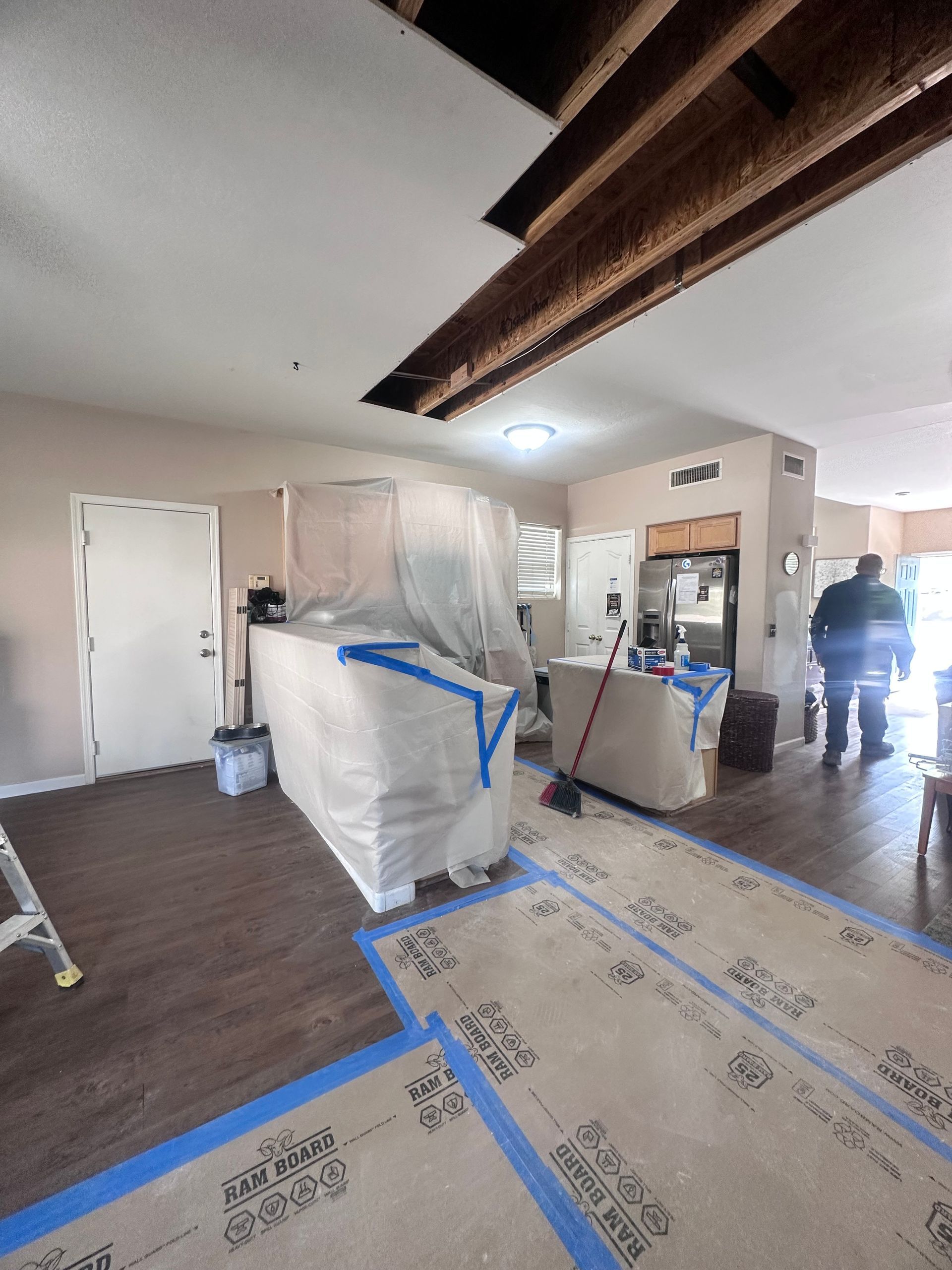 Room with exposed ceiling beams, plastic-covered countertops, and a person in the background.