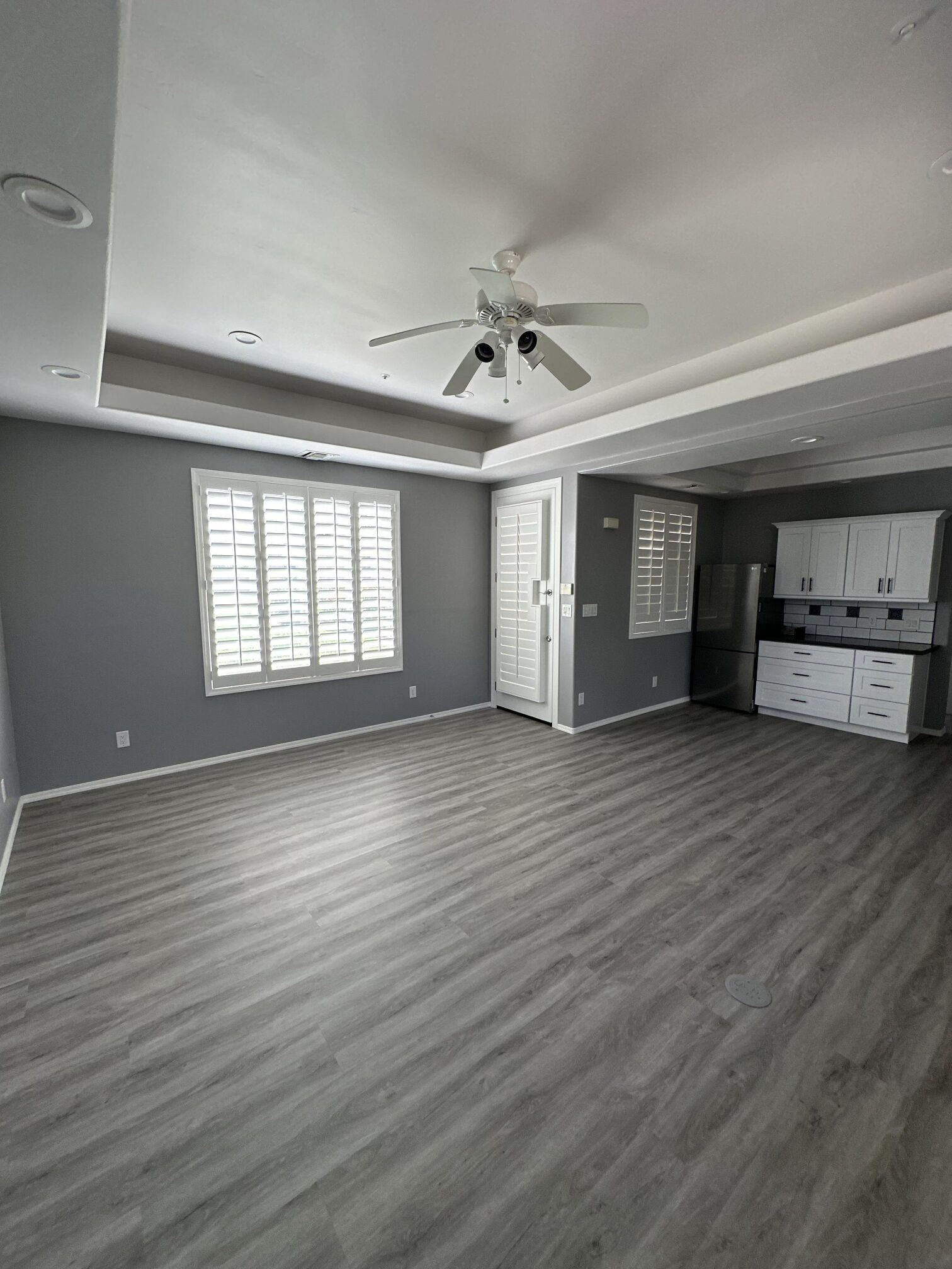 Empty living room with grey walls, flooring, and ceiling. White trim, shutters, and cabinets.